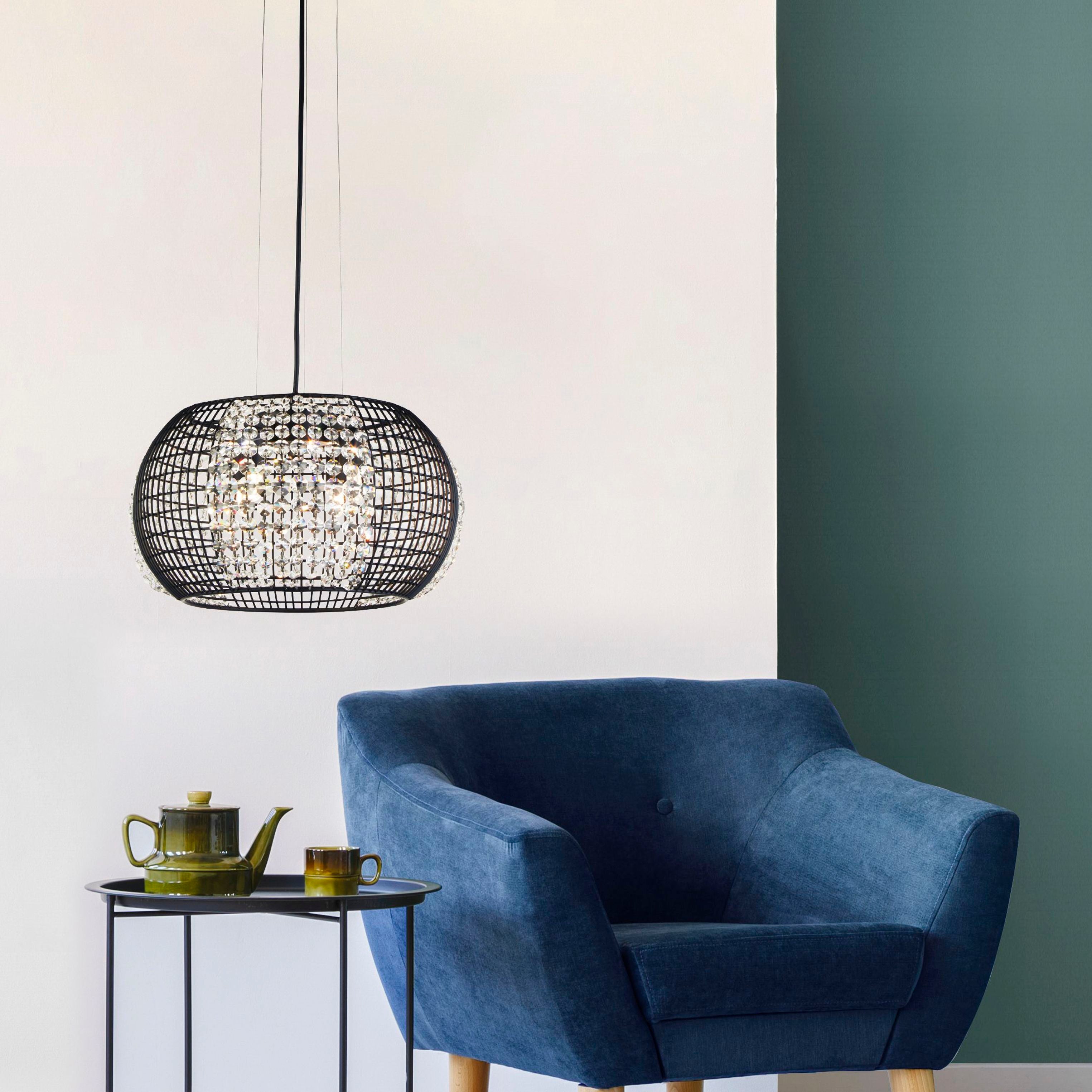 Cage 4 light pendant styled above a dark side table next to a blue velvet armchair in a green and white living room