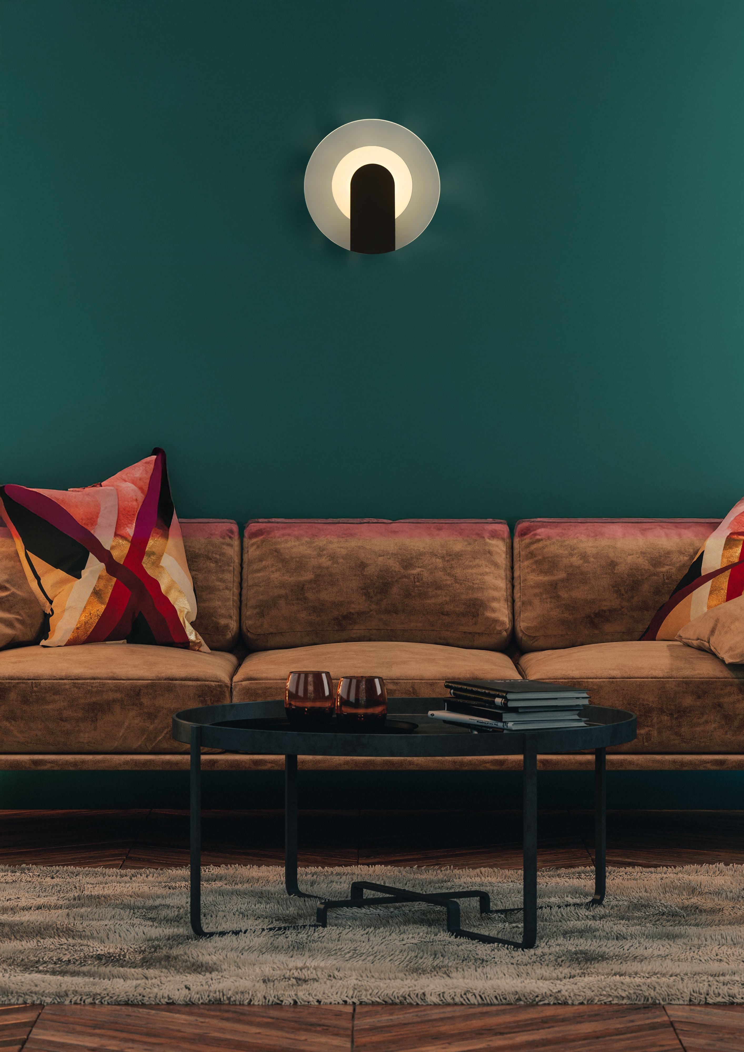 Target wall light lit and mounted on a deep red textured wall above a small shelf with a potted olive tree and candle