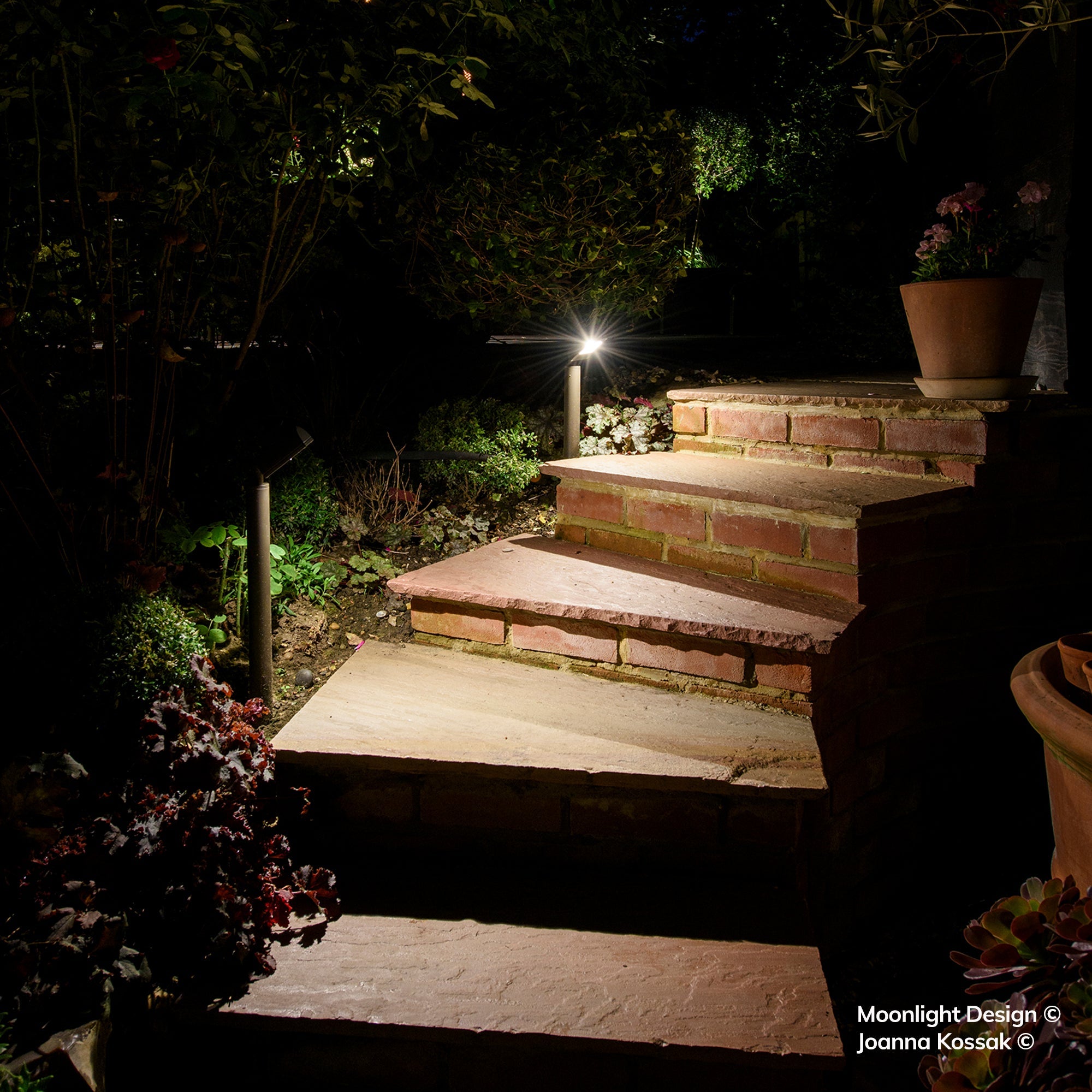 Two Hunza Border Lights either side of brick and stone steps leading up to a patio at night, Moonlight Design garden lighting