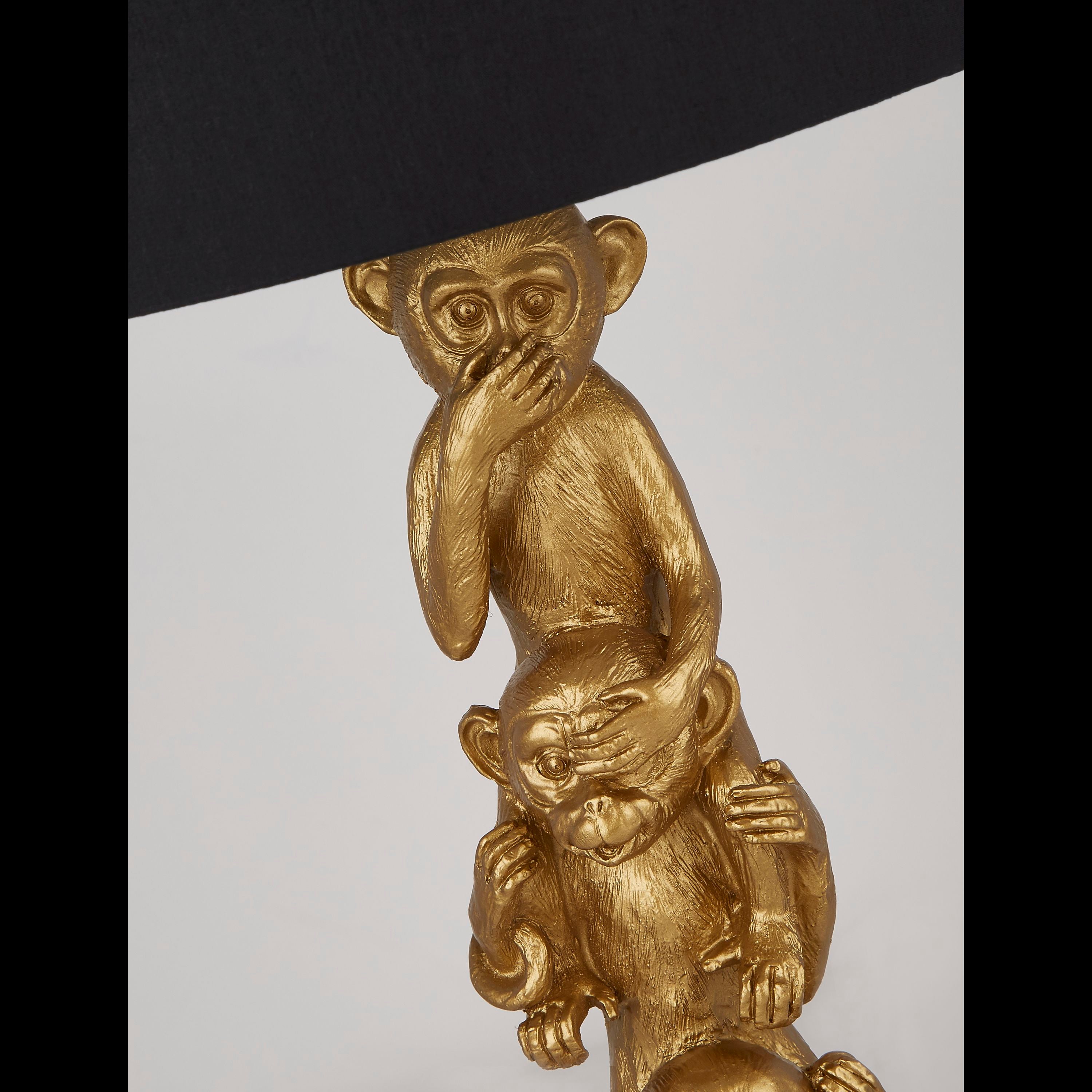 Close up of the gold resin monkey figures on the 3 Wise Monkeys table lamp, showing hands covering the eyes and mouth in the see no evil, hear no evil, speak no evil pose