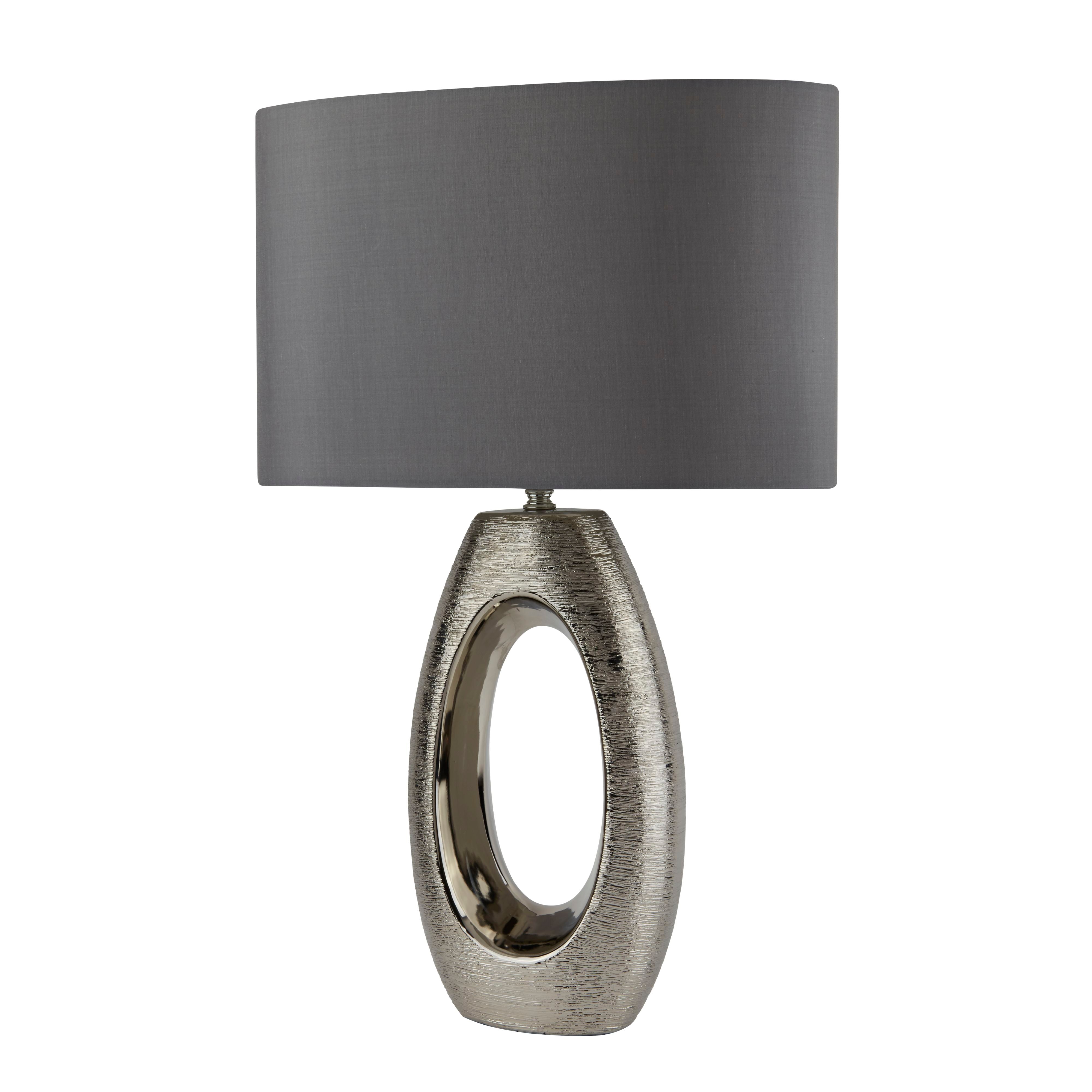 Searchlight Artisan table lamp with brushed silver oval cut out ceramic base and grey faux silk shade, straight on studio shot on a white background