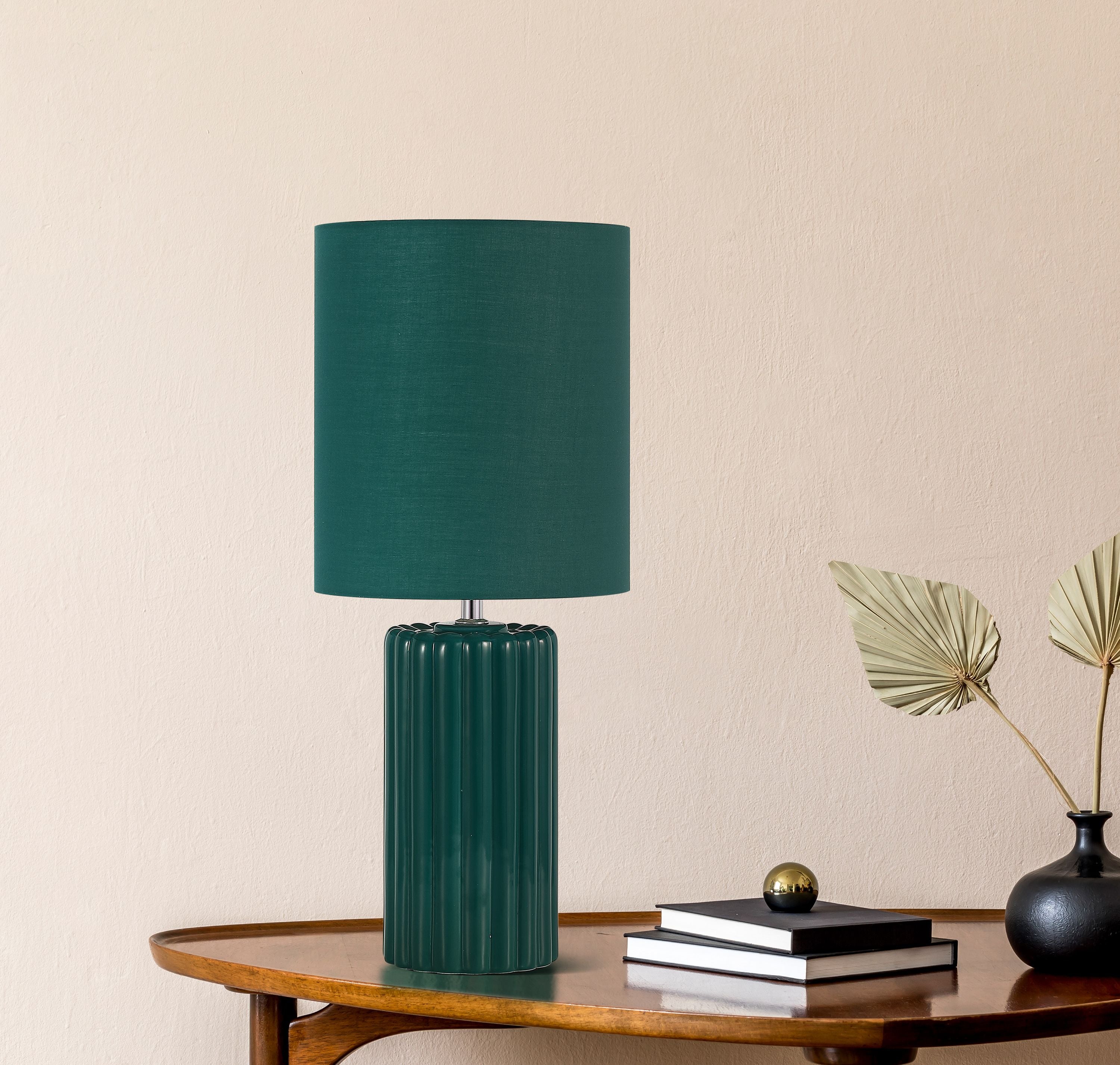 Groove olive green table lamp styled on a wooden console table beside a stack of books, a small brass ornament and a dried palm frond