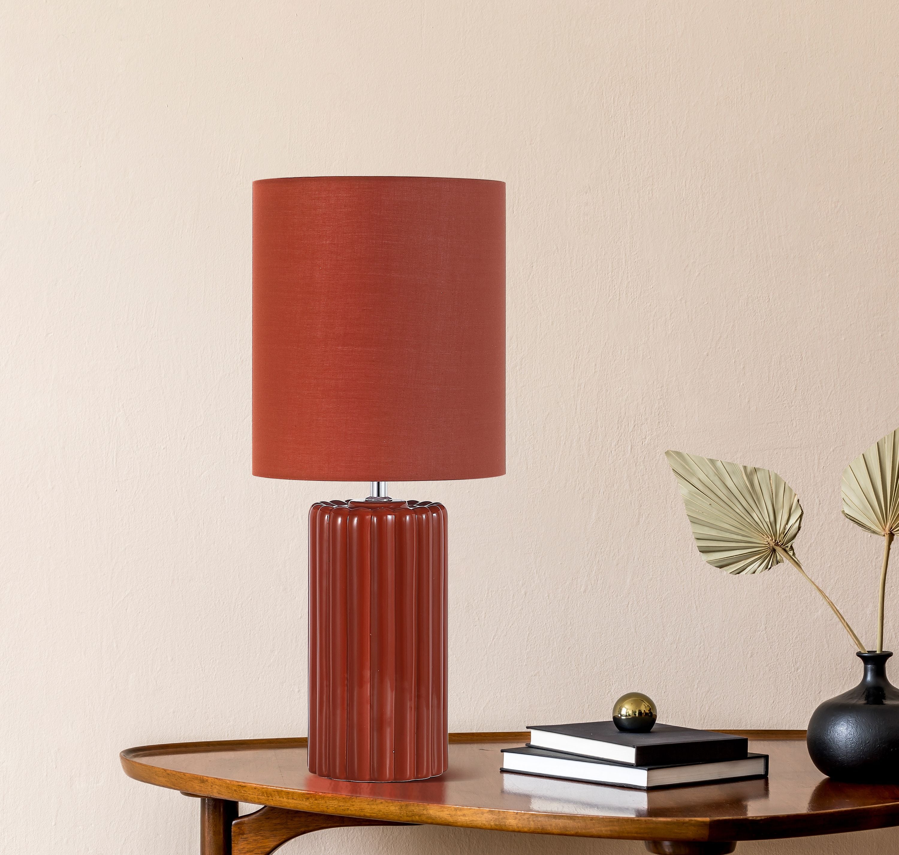 Groove burnt orange table lamp styled on a wooden console table beside a stack of books, a small brass ornament and a dried palm frond