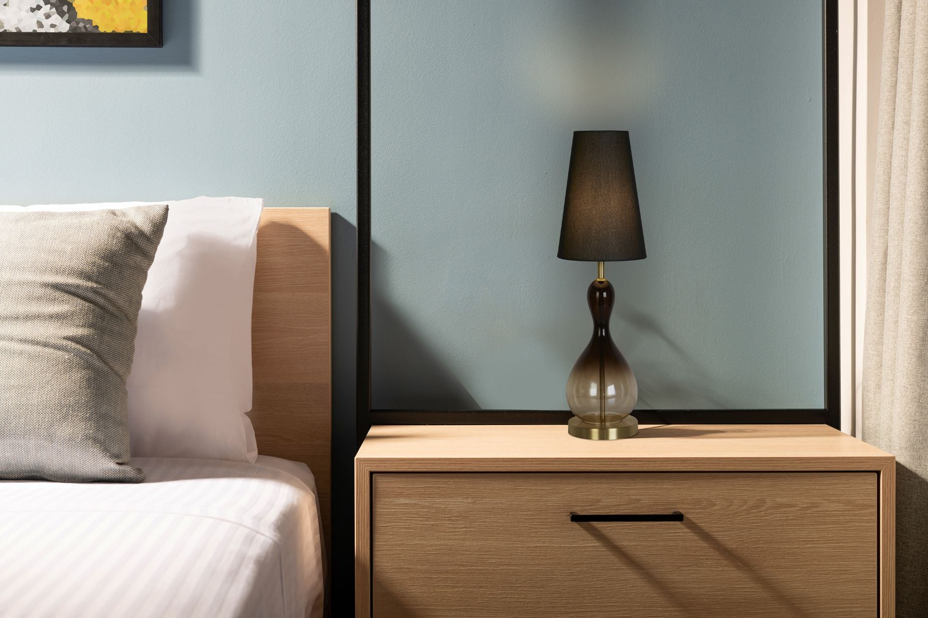 Marakesh table lamp styled on a cream bedside cabinet in front of a mirror, lit and casting a warm glow in a bedroom setting