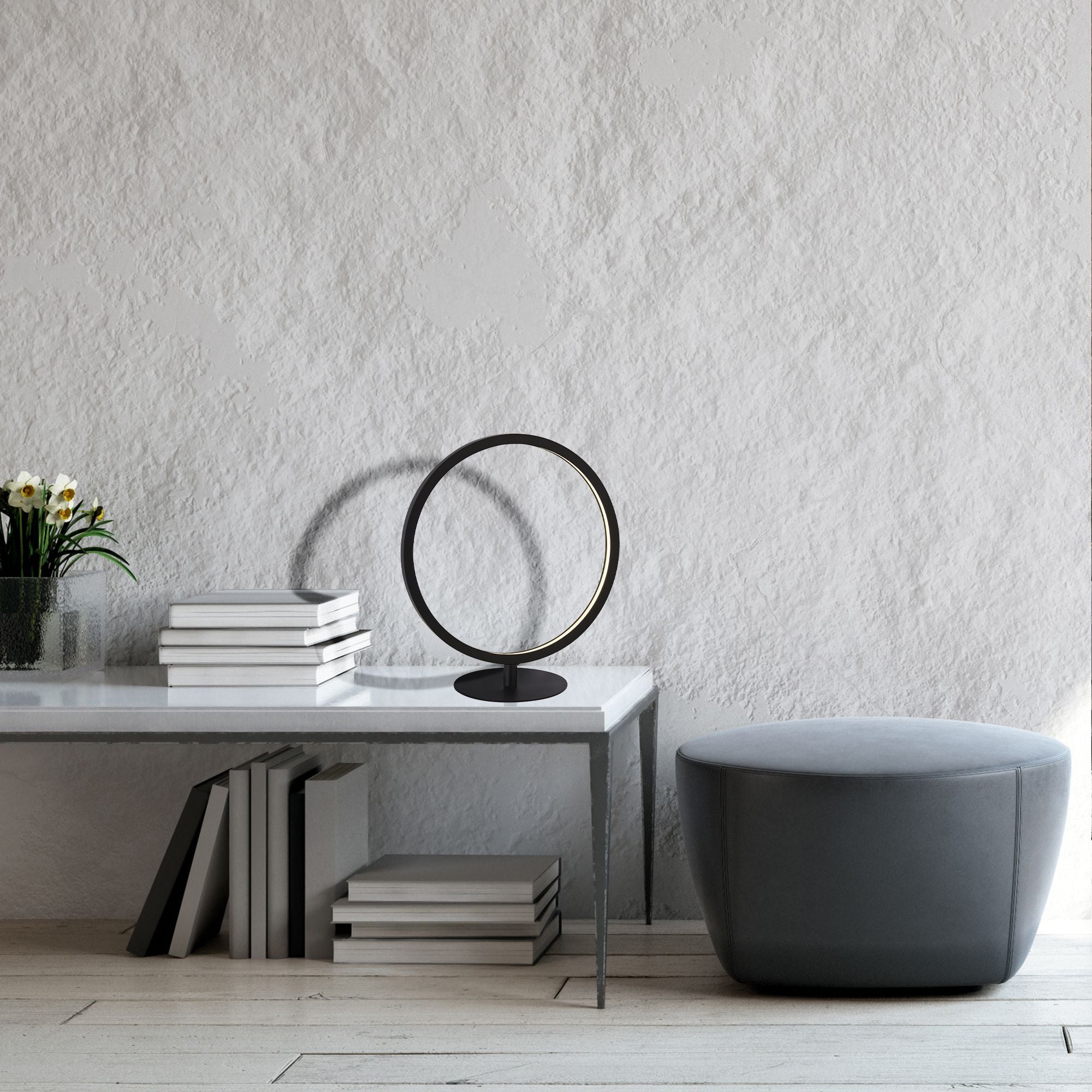 Searchlight Cirque ring table lamp styled on a white side table with a stack of books, a small vase of flowers and a grey ottoman nearby