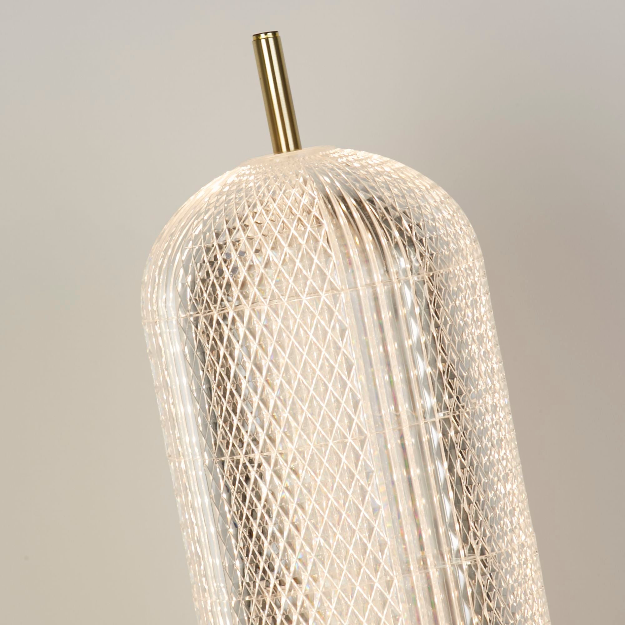 Close up of the Capsule table lamp's faceted acrylic shade and brass stem, showing the diamond lattice texture lit from within