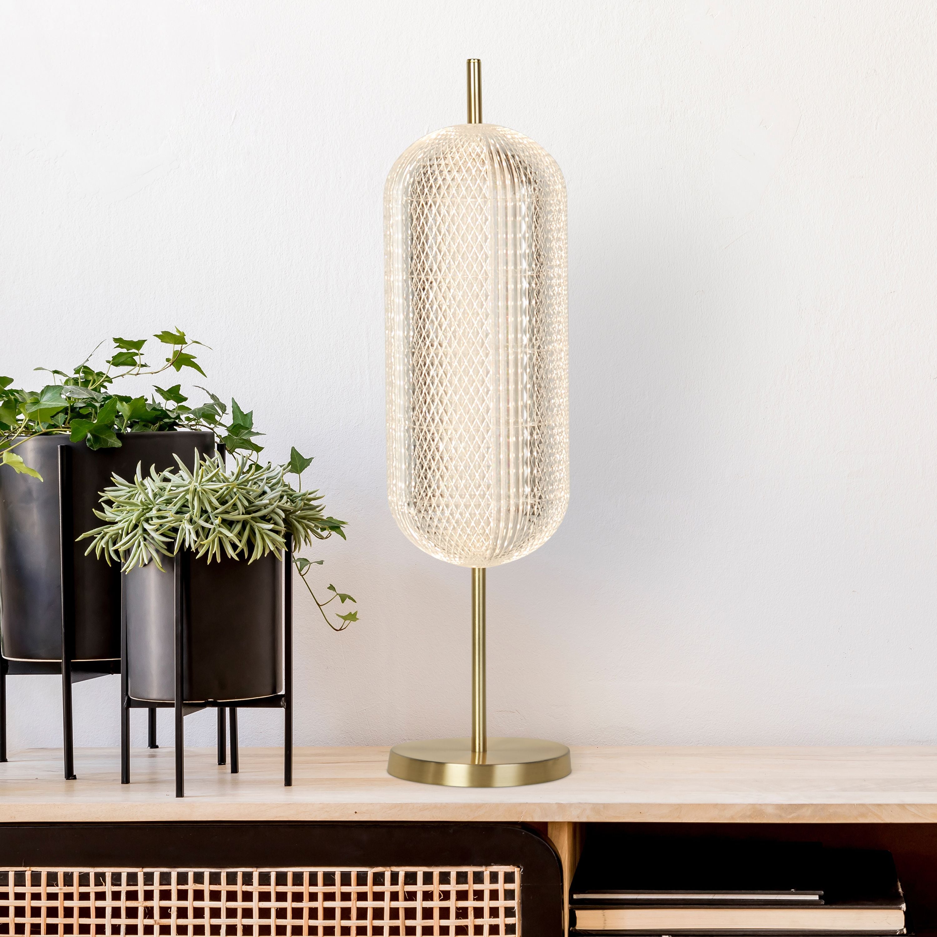 Searchlight Capsule LED table lamp in satin brass styled on a sideboard beside potted plants in dark planters