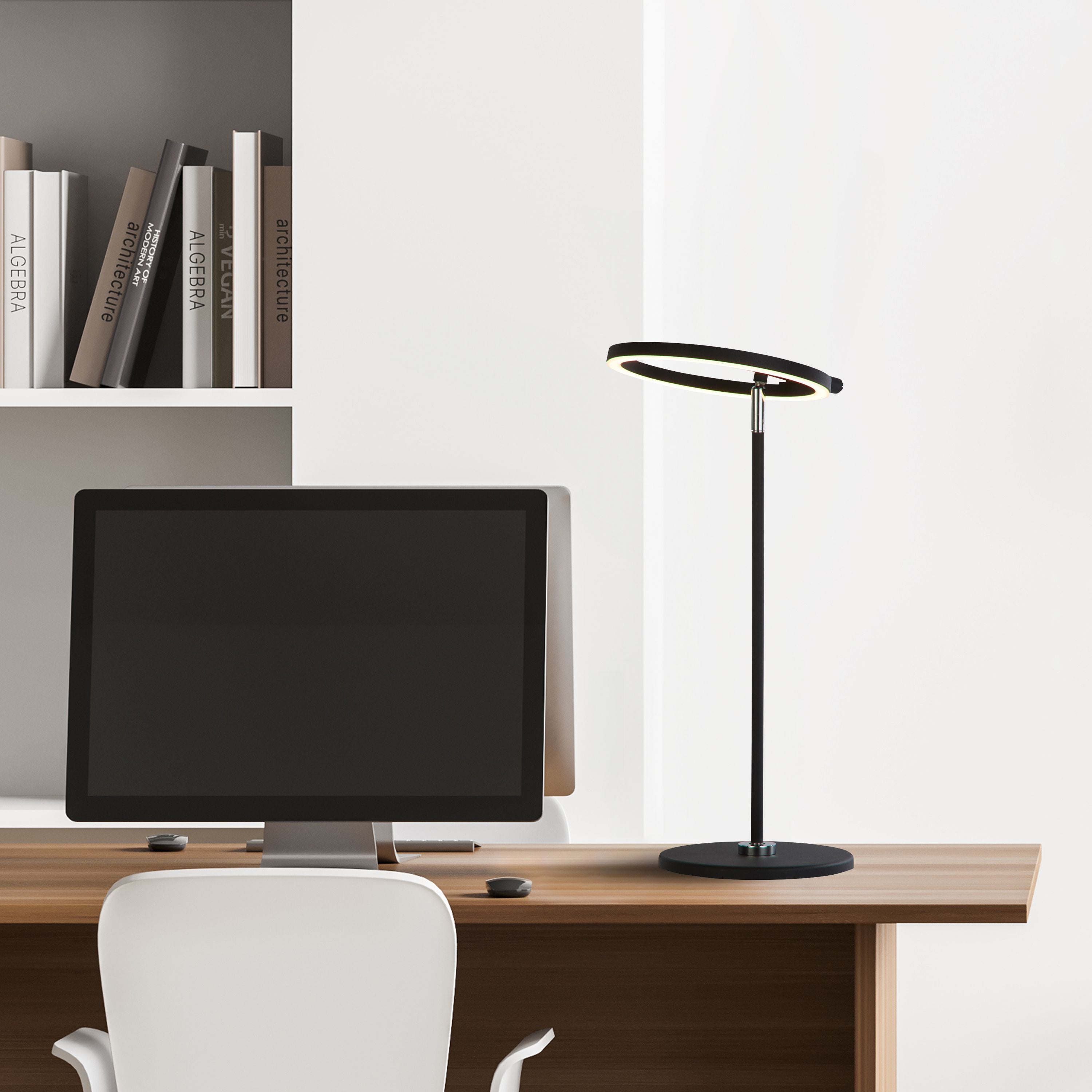 Searchlight Space LED table lamp in black styled on a desk beside a computer monitor and bookshelf, illuminated with a warm glow