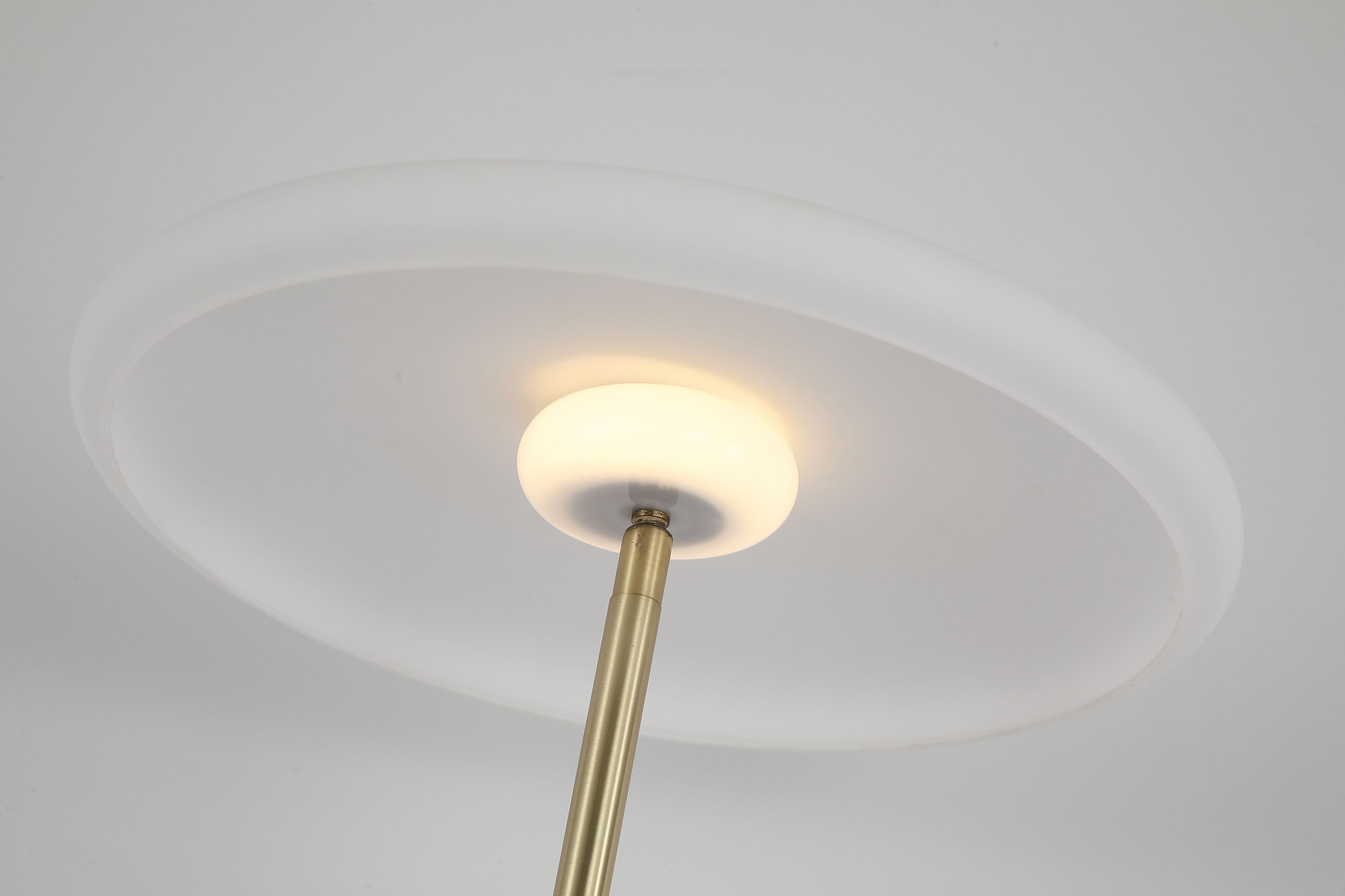 Close up from below of the Record floor lamp's illuminated white glass shade and satin brass column
