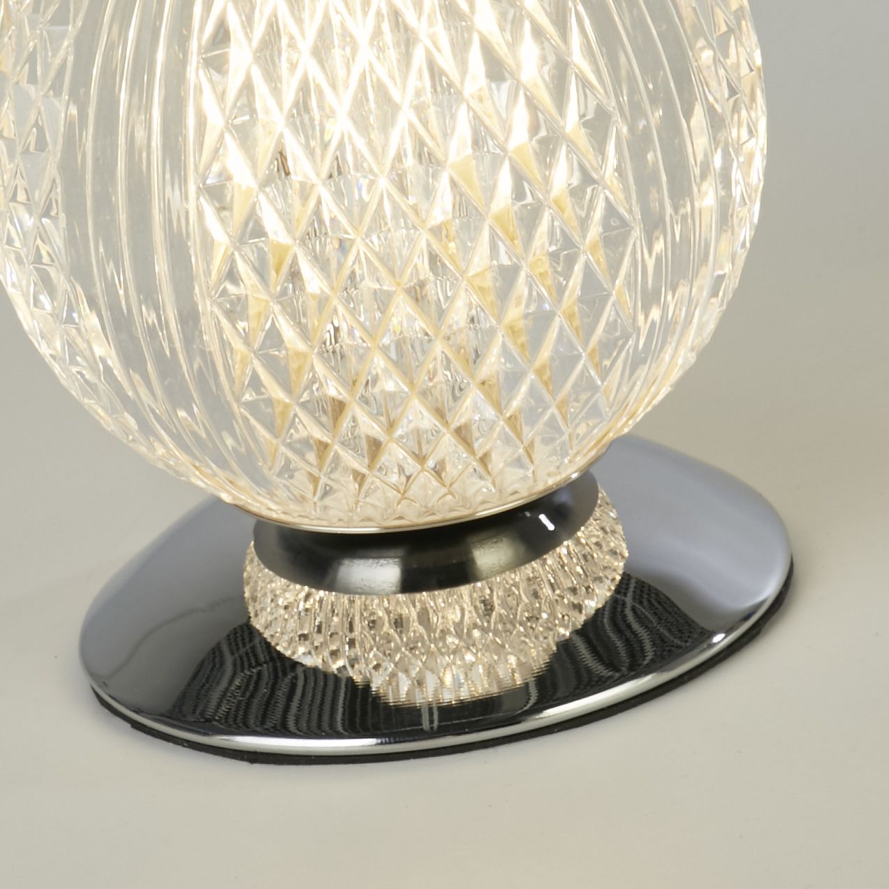 Close up of the Allure table lamp's chrome base, showing the ridged texture where the acrylic globe meets the polished metal cap