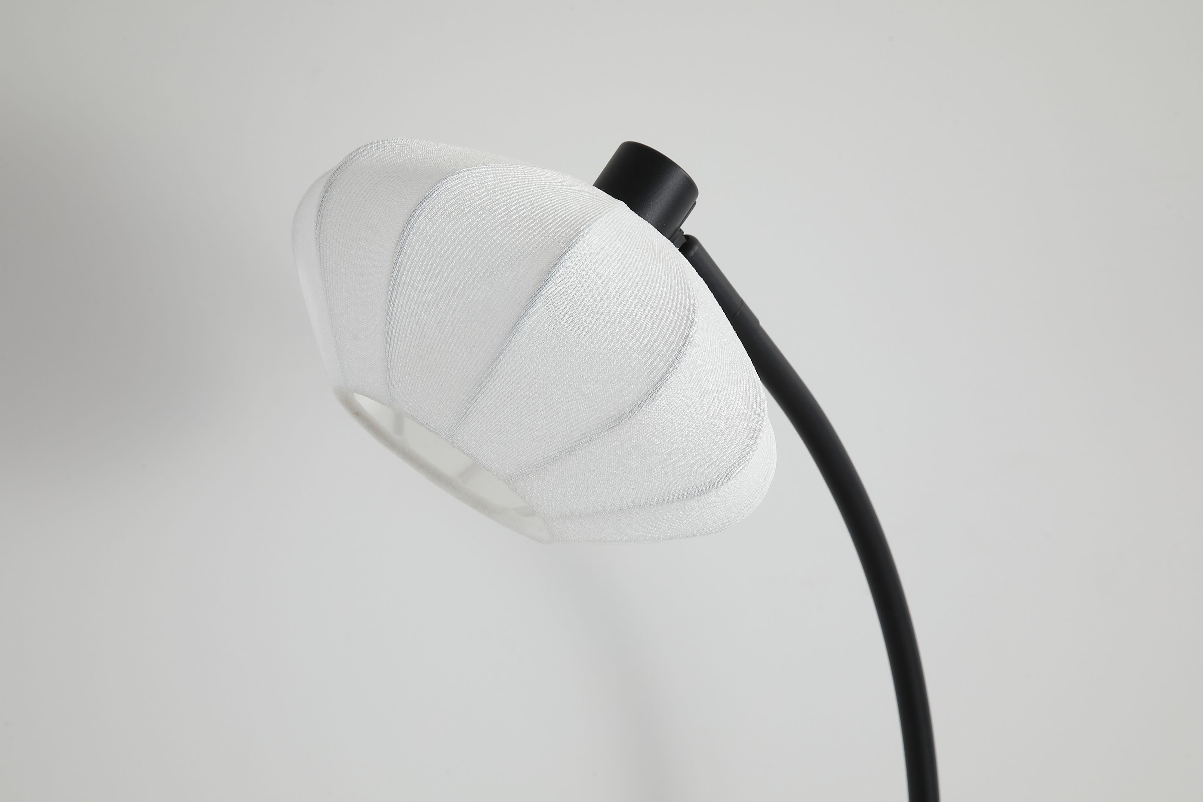 Close up of the Radiant table lamp's bud shaped shade and black gimbal joint at the top of the curved arm