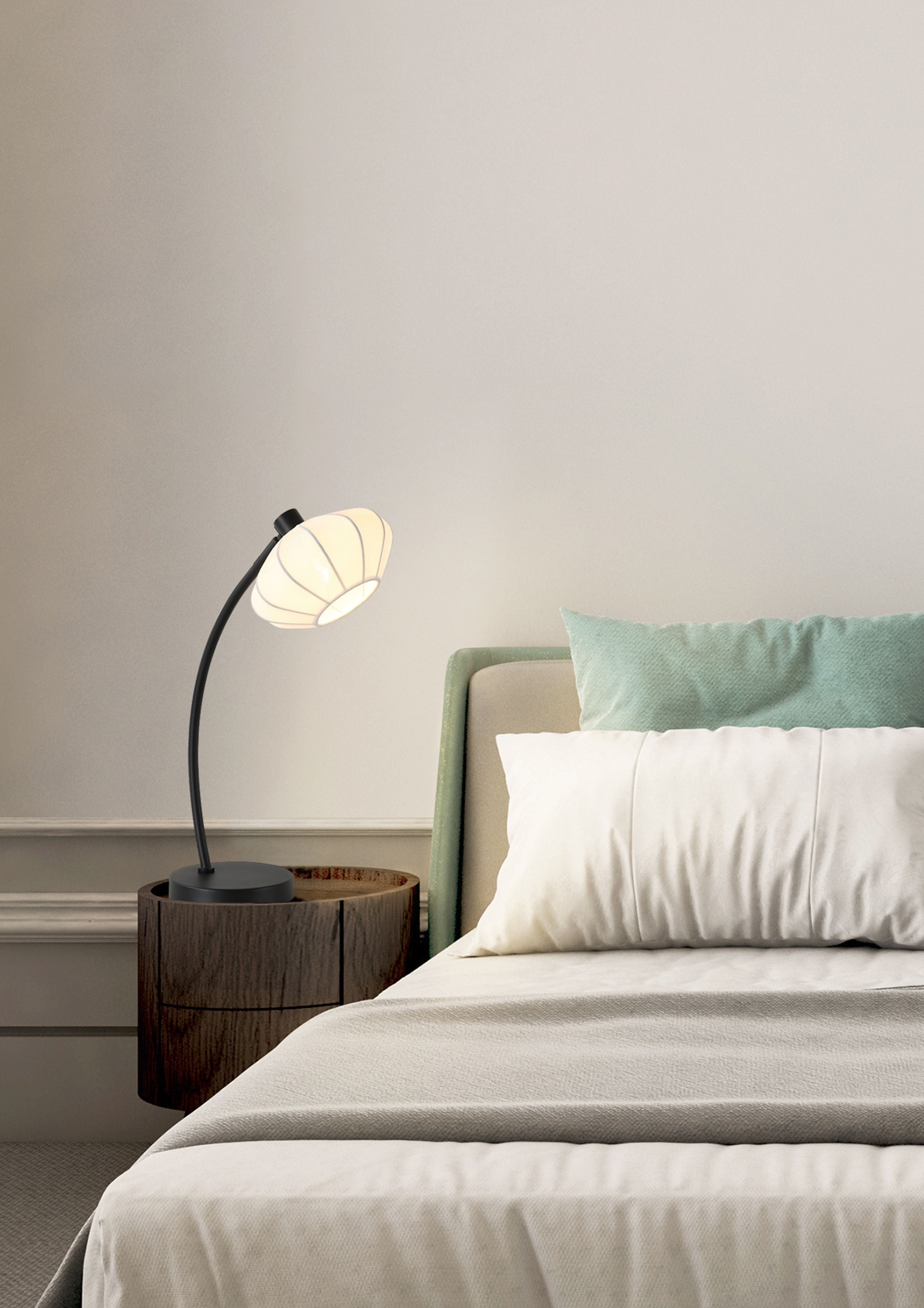 Radiant table lamp lit on a dark wood bedside table beside a bed with teal cushions