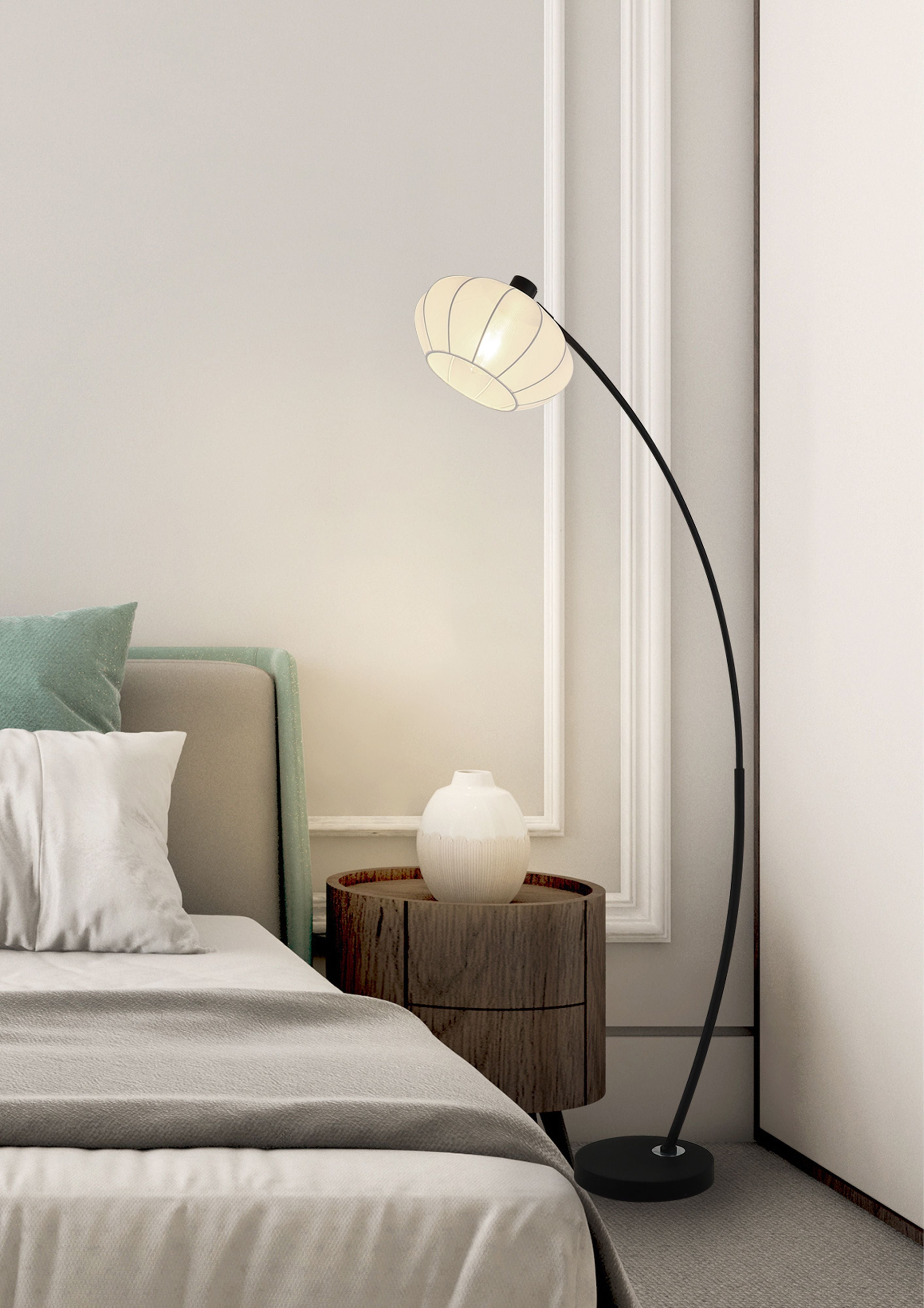 Radiant floor lamp arching over a bedside area, lit beside a bed with teal cushions and a dark wood side table