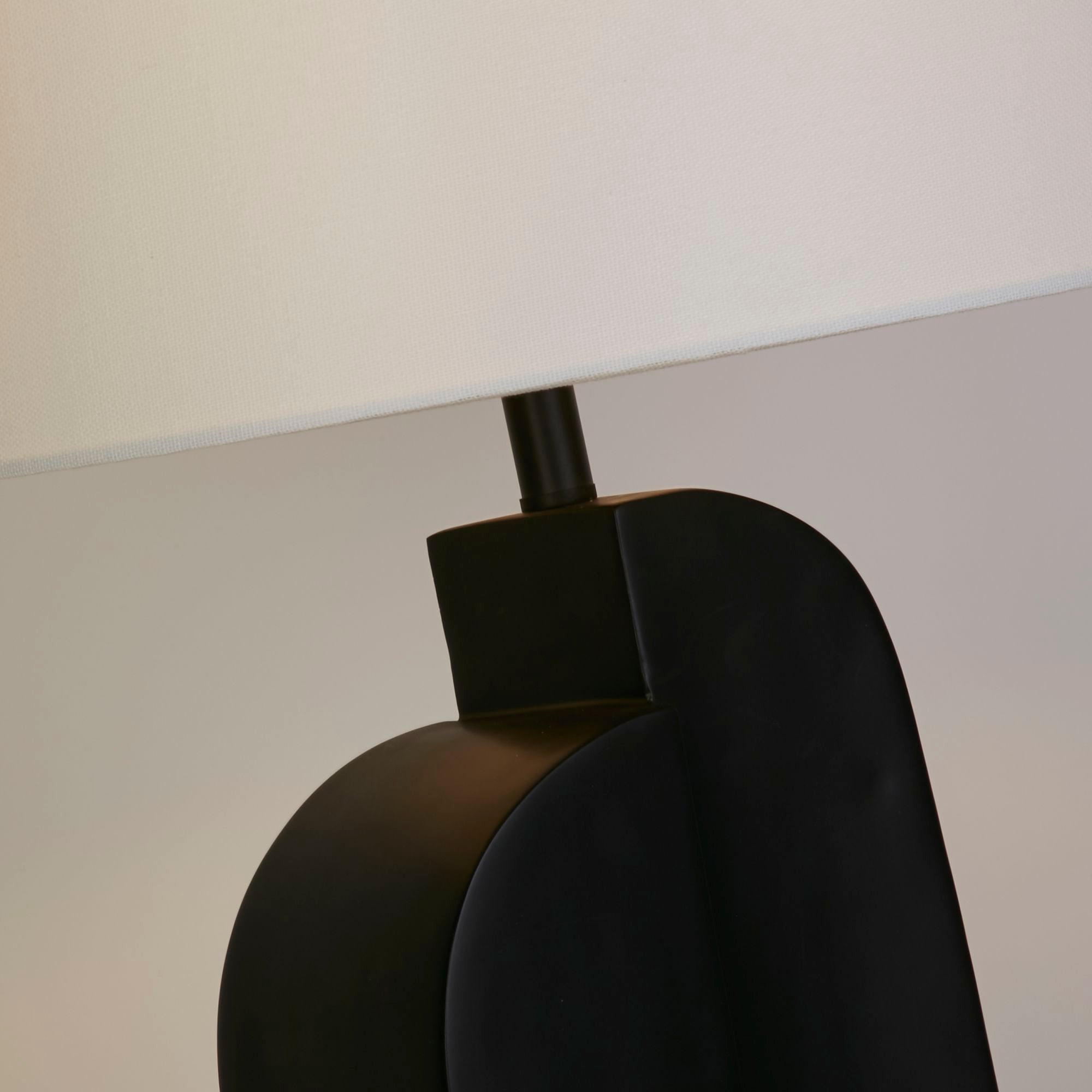 Close up of the Perth table lamp base and shade join, showing the matt black arch shaped base and the underside of the white linen shade