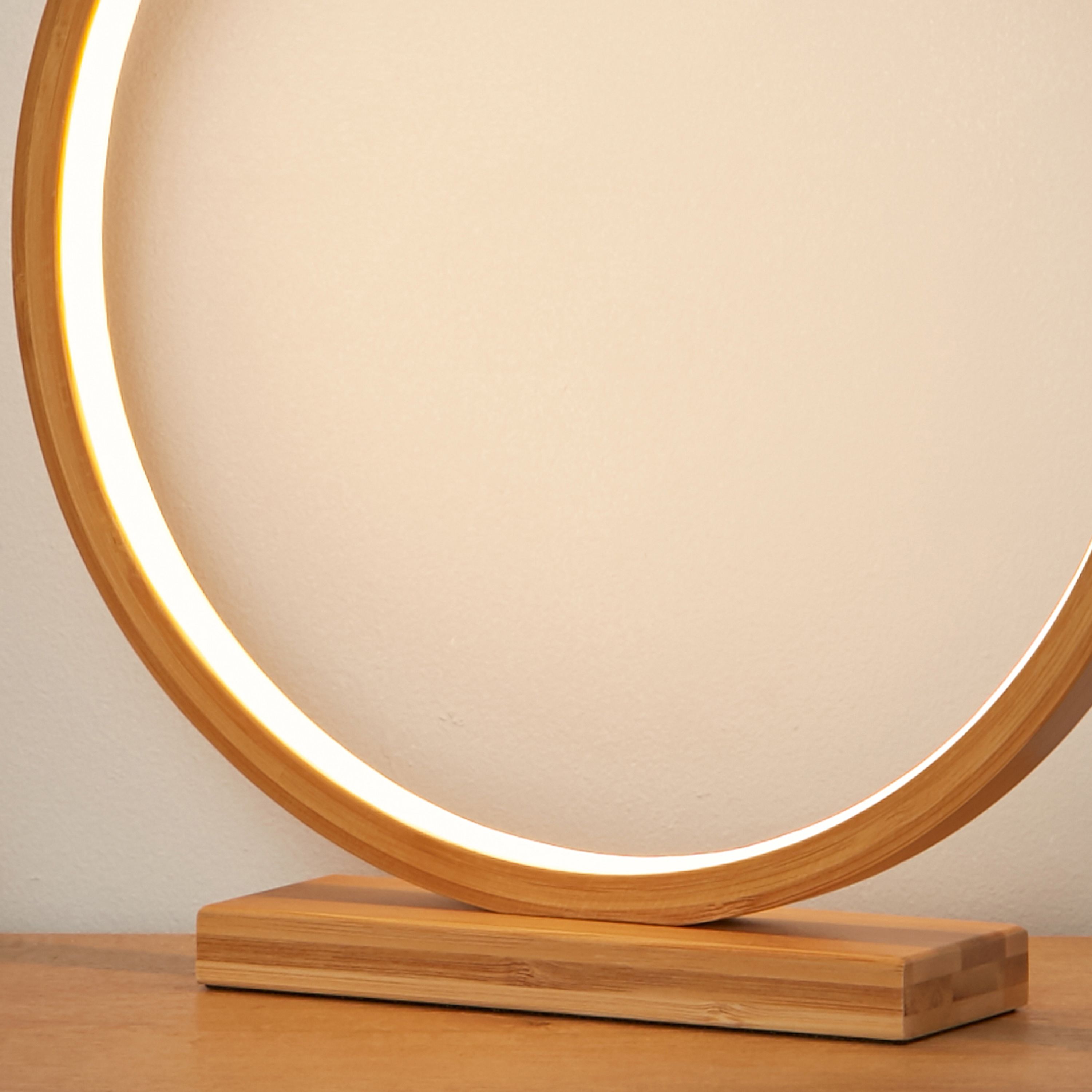 Close up of the lit bamboo ring on the Malibu LED table light, showing the warm white glow along the inner edge and the wood grain detail