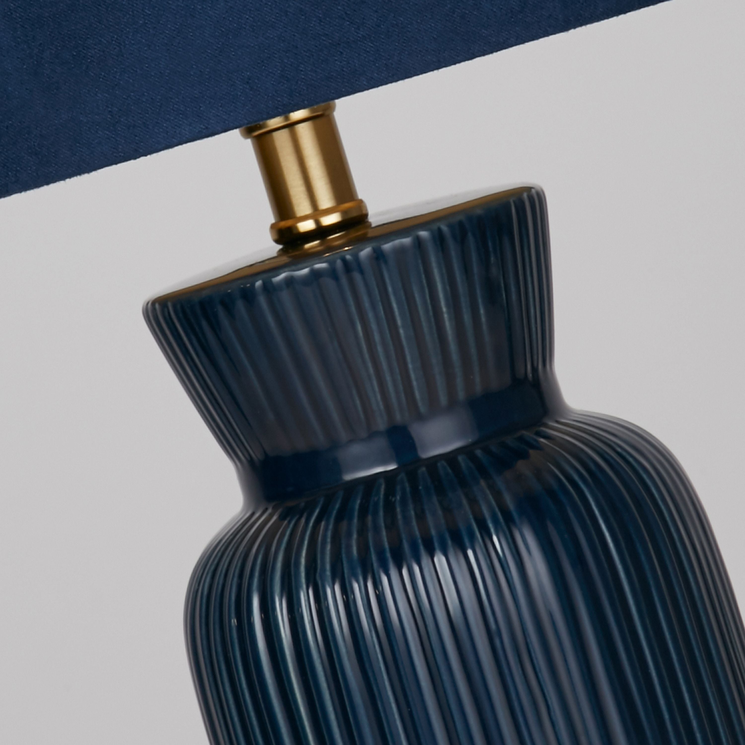 Close up of the navy ceramic table lamp's fluted neck and brass gallery fitting beneath the drum shade