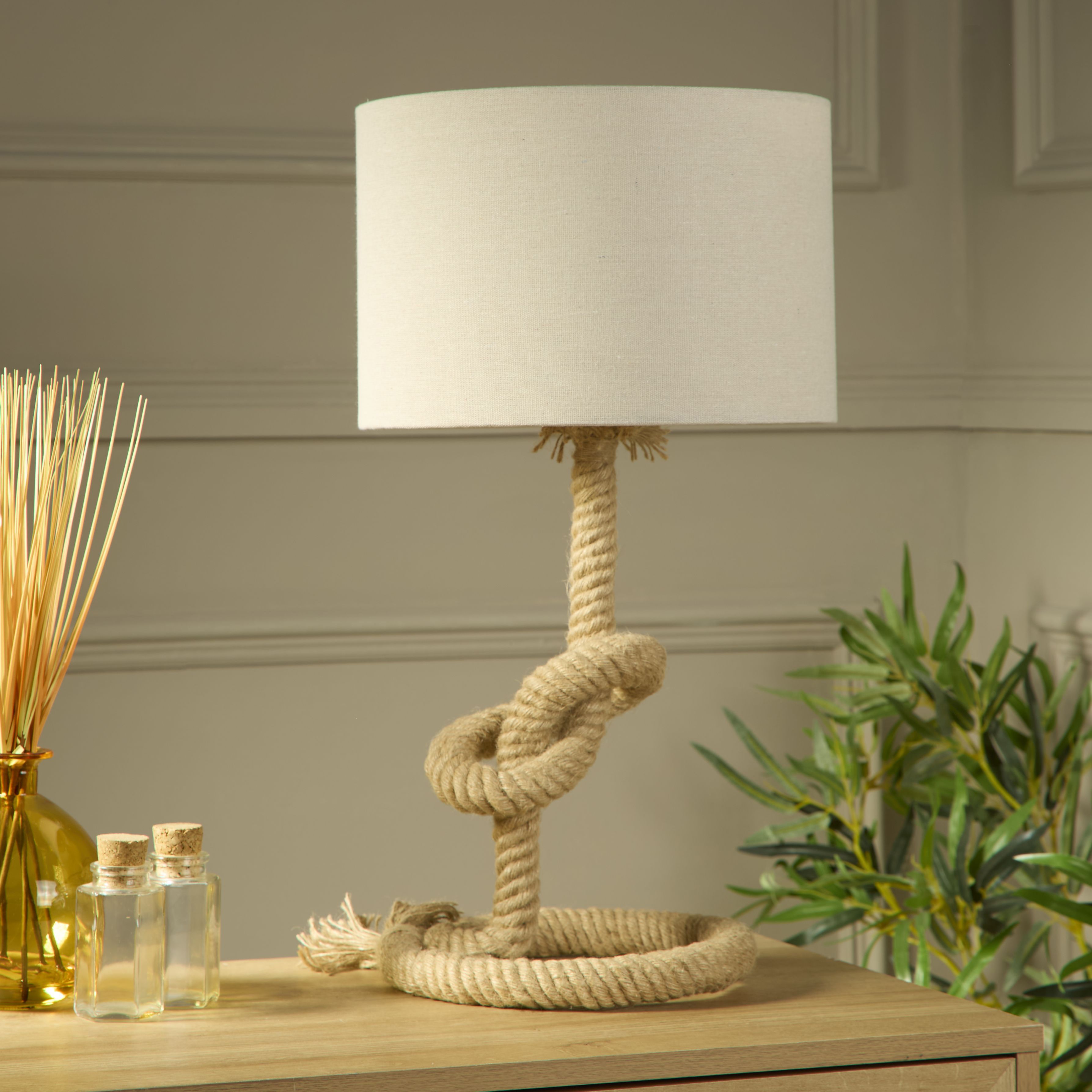 Searchlight Rope table lamp styled on a wooden sideboard with a plant diffuser and reed sticks, lit lifestyle shot