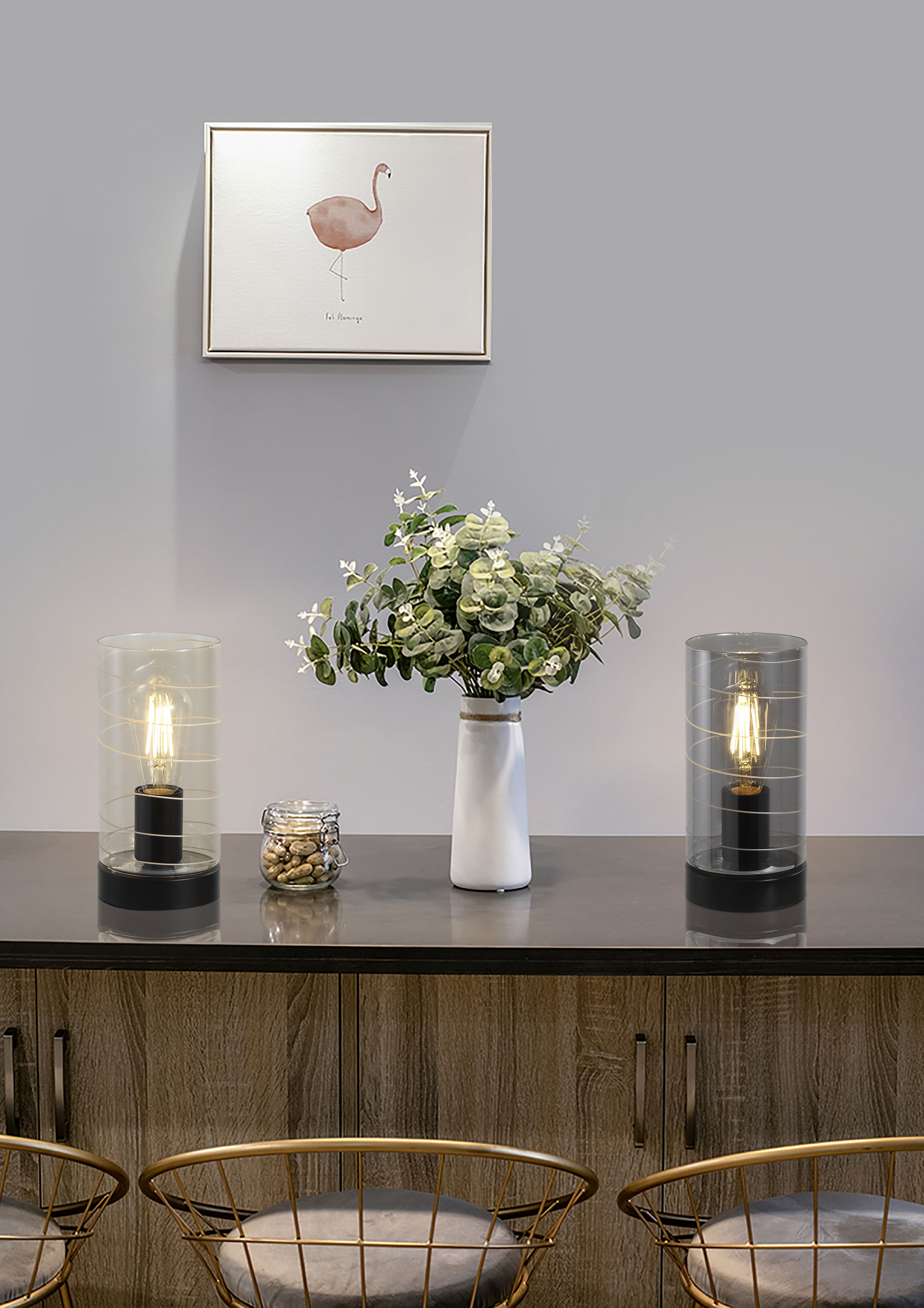 Broughton table lamps in amber and smoked glass styled together on a sideboard beneath a flamingo print, both lit with visible filament bulbs