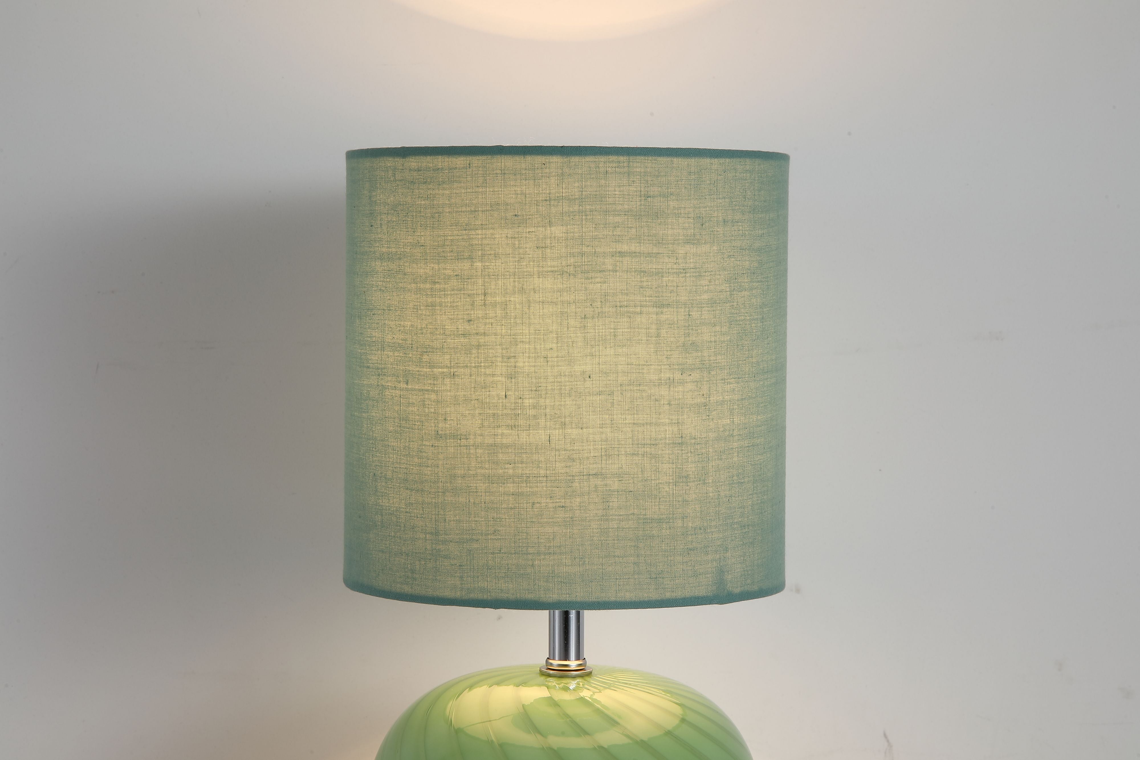 Extreme close up of the Fete lamp's green linen shade fabric and top edge, cropped tight against a plain grey background