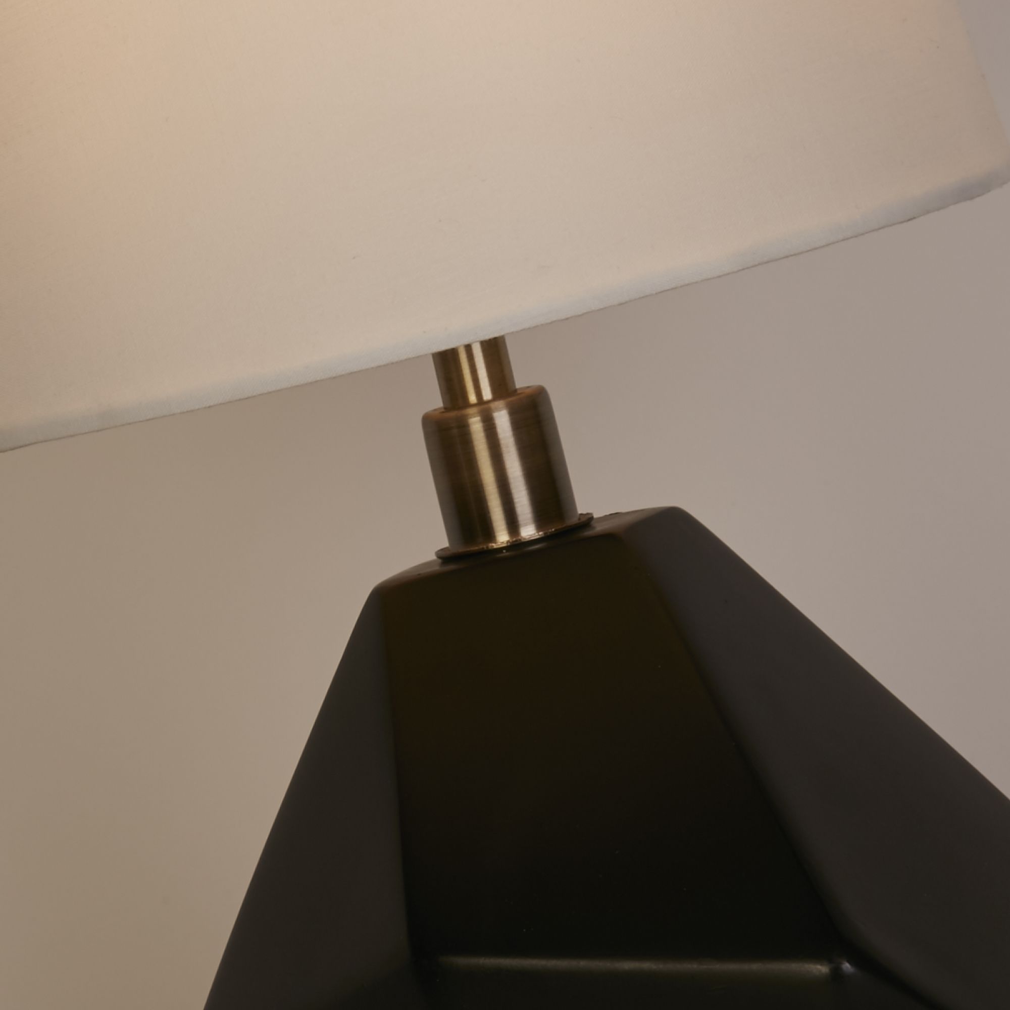 Close up of the Apex table lamp neck showing the antique brass fitting against the black faceted base