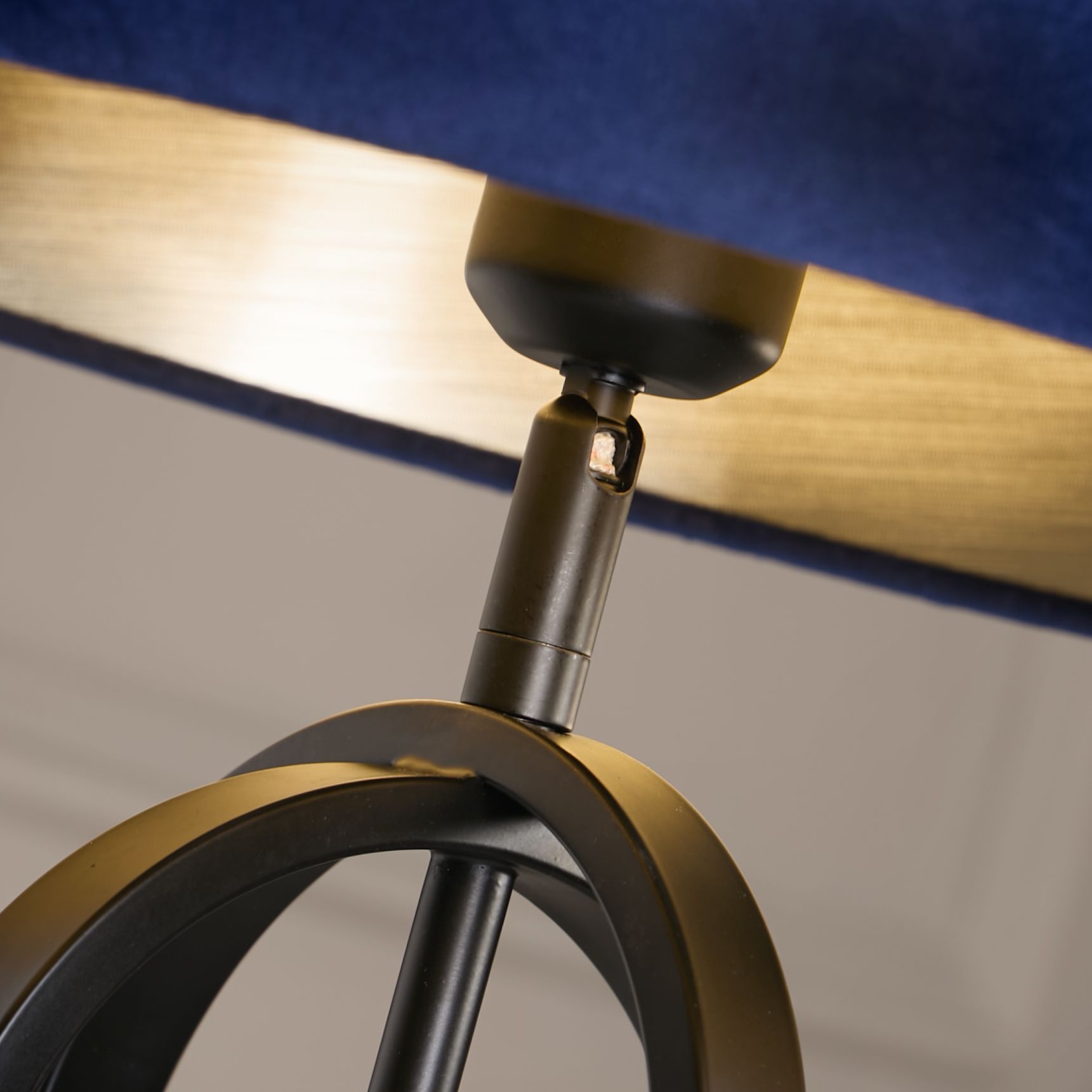 Close up of the lamp's bronze toned adjustable joint connecting the fitting to the black interlocking oval frame, with the navy velvet shade visible above