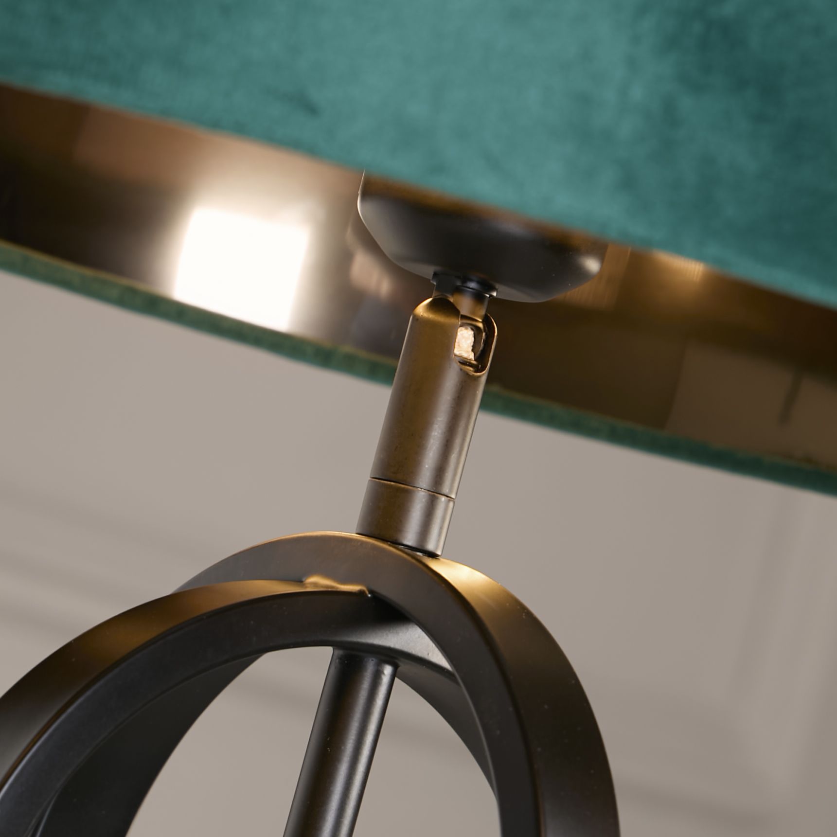 Close up of the lamp's bronze toned adjustable joint connecting the fitting to the black interlocking oval frame, with the emerald velvet shade visible above