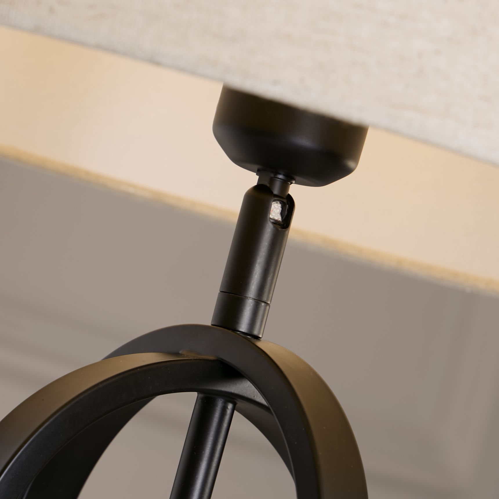 Close up of the lamp's bronze toned adjustable joint connecting the fitting to the black interlocking oval frame, with the natural linen shade visible above