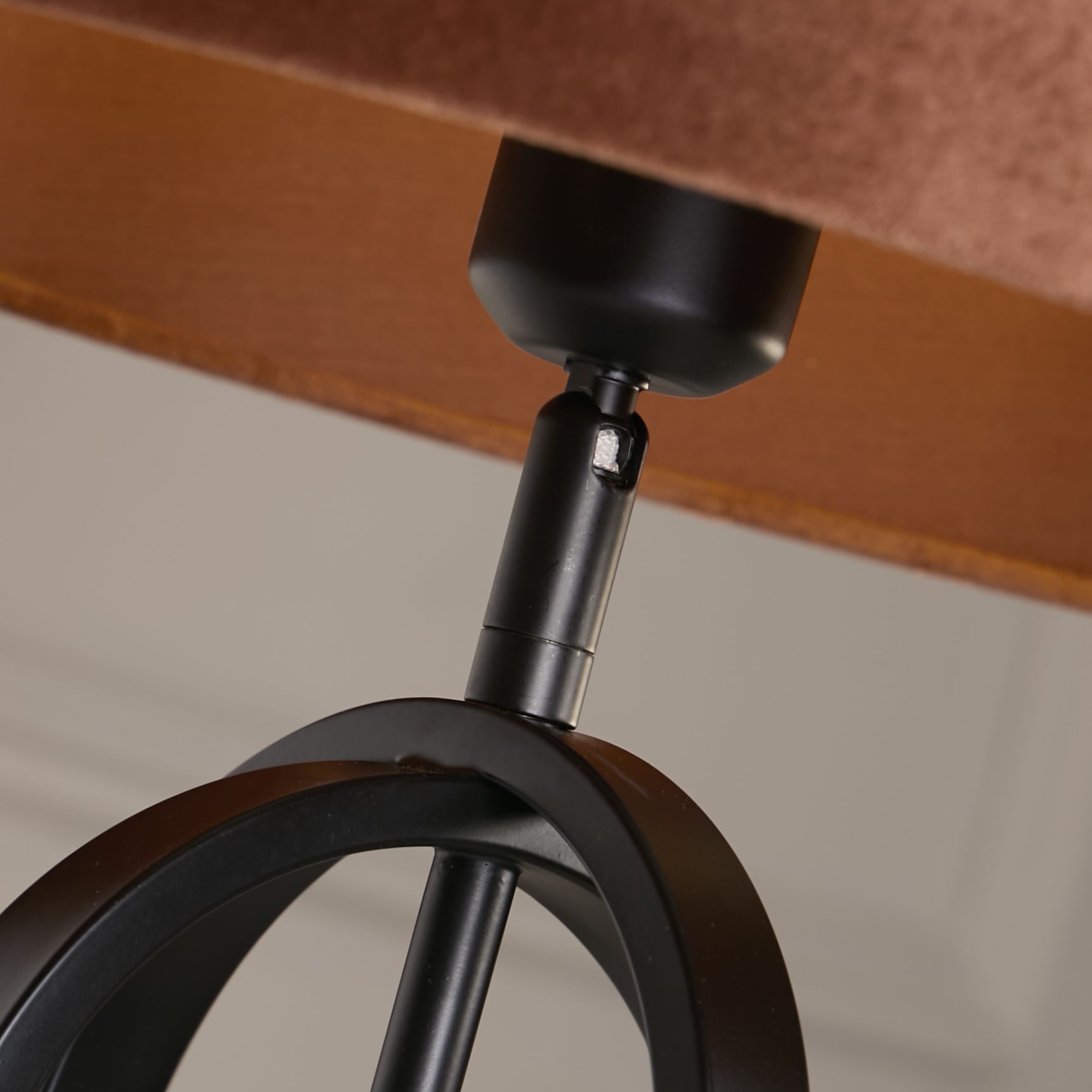 Close up of the lamp's bronze toned adjustable joint connecting the fitting to the black interlocking oval frame, with the burnt orange velvet shade visible above
