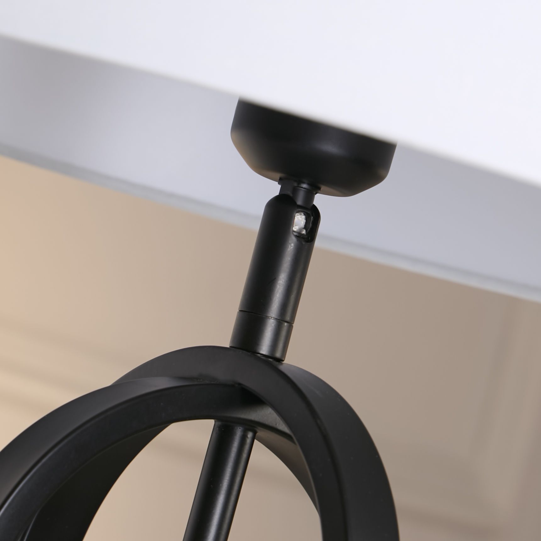 Close up of the lamp's bronze toned adjustable joint connecting the fitting to the black interlocking oval frame, with the white shade visible above