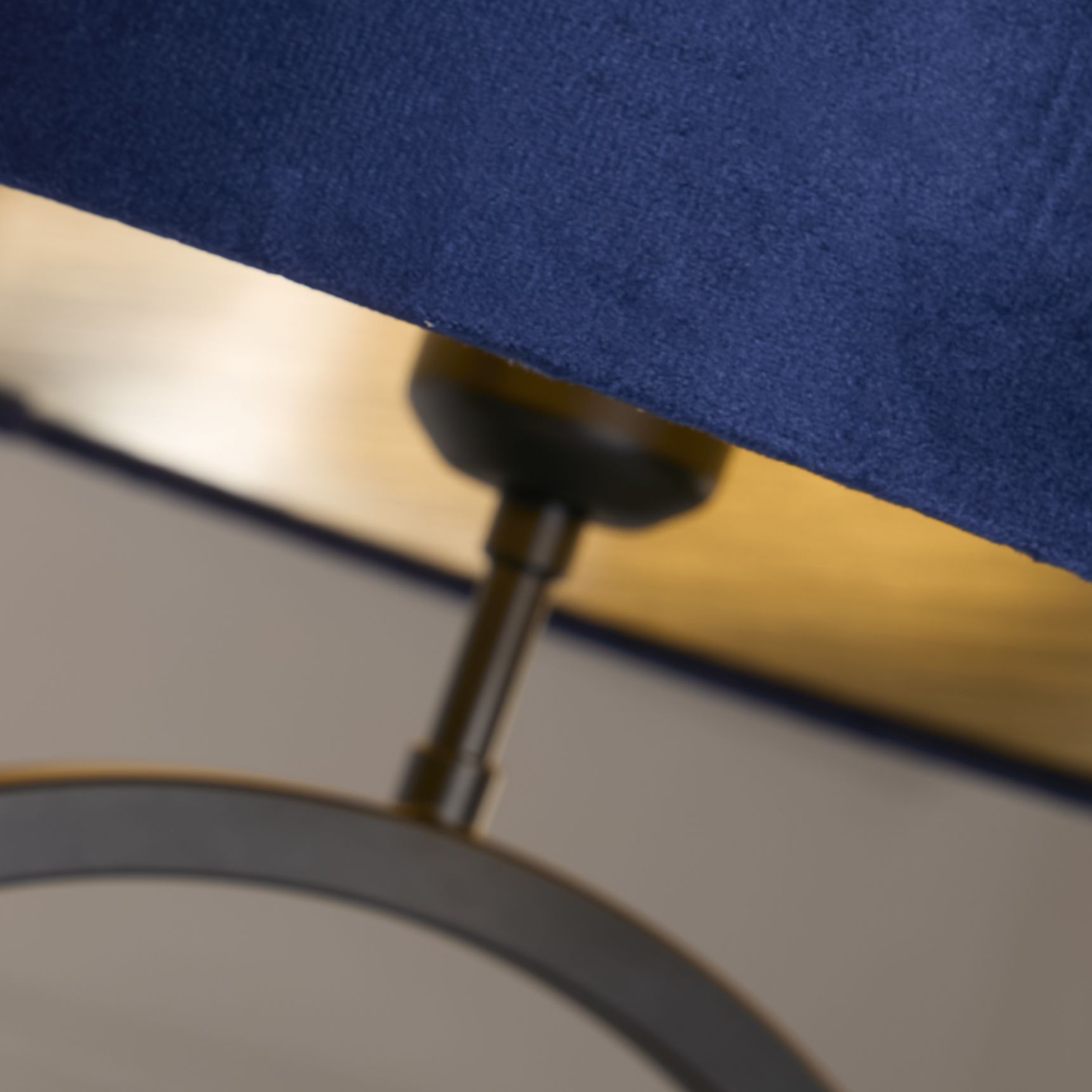 Close up of the brass coloured collar joint connecting the navy velvet shade to the matt black ring base