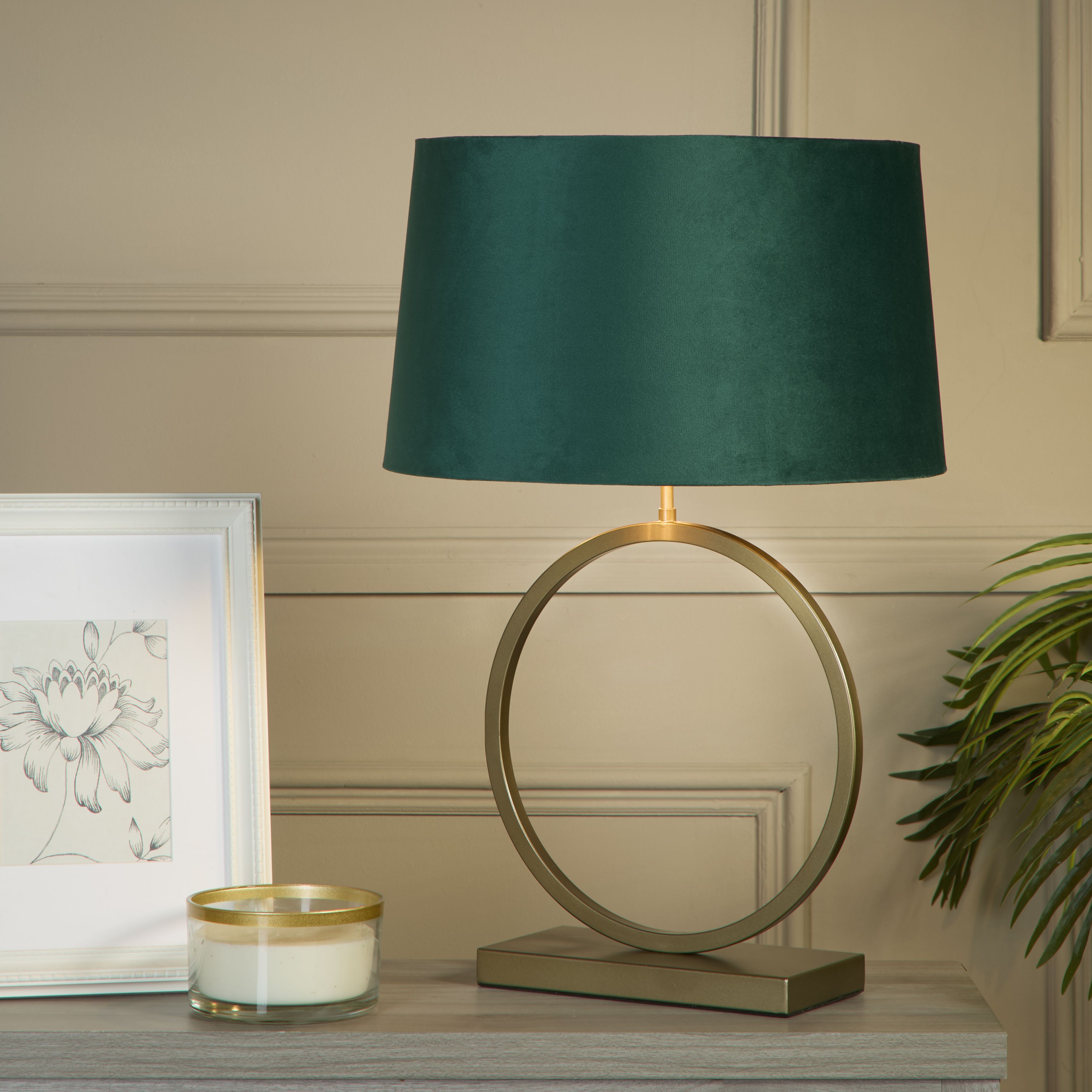 Elegant table lamp with emerald velvet shade styled on a console table with a framed botanical print, candle and trailing plant