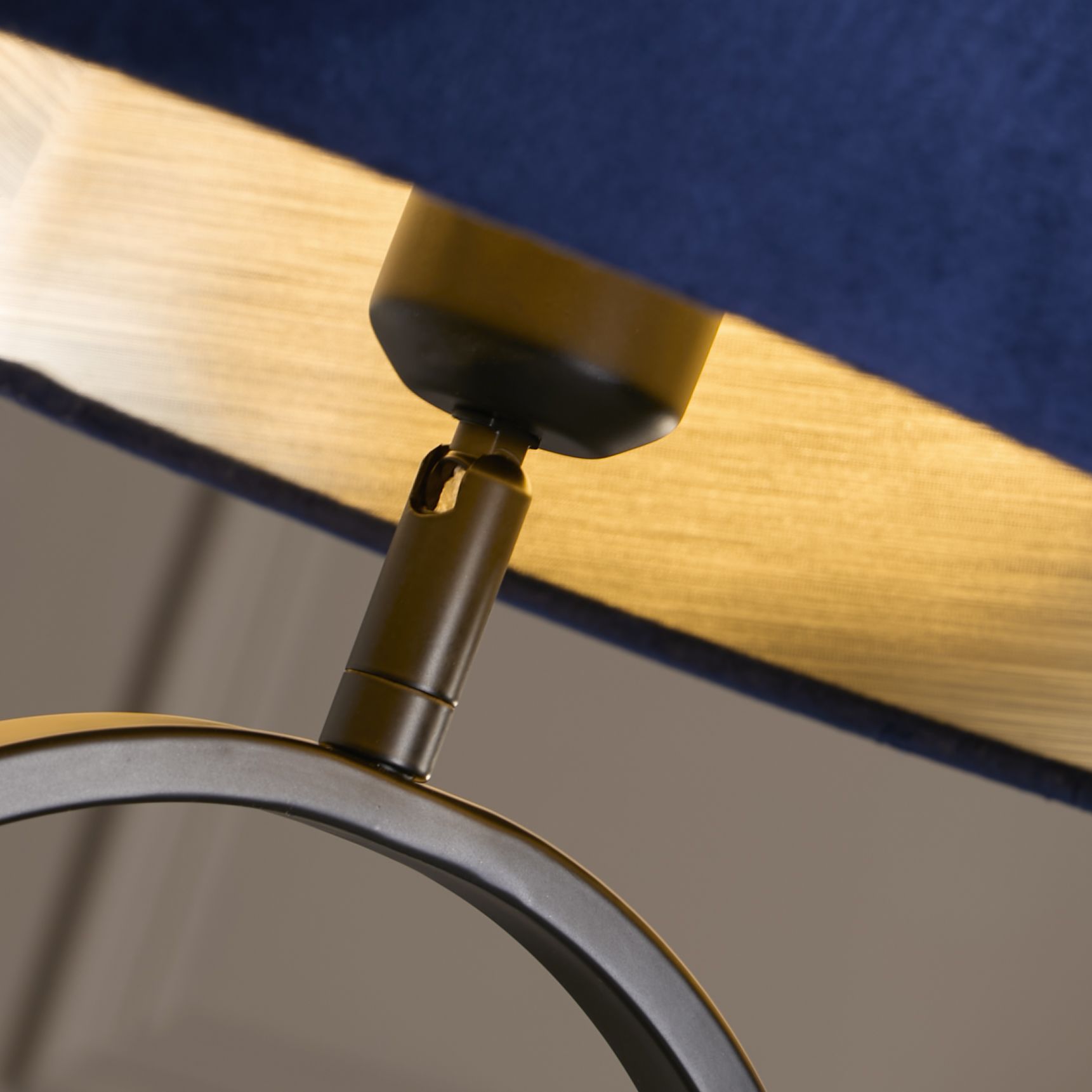 Close up of the Modish table lamp's brass toned finial and lamp holder where the navy velvet shade meets the black metal base.
