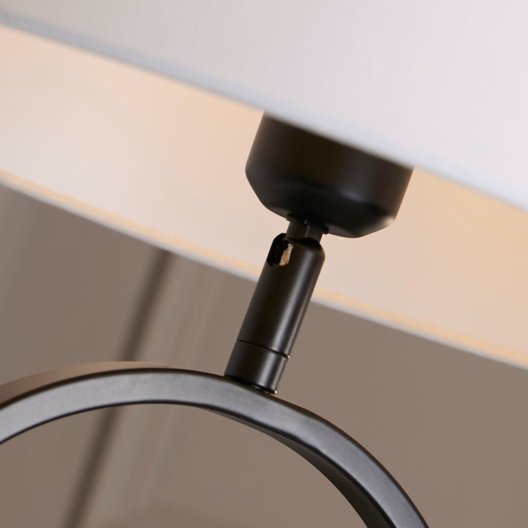 Close up of the brass adjustable joint connecting the white cotton shade to the matt black oval base