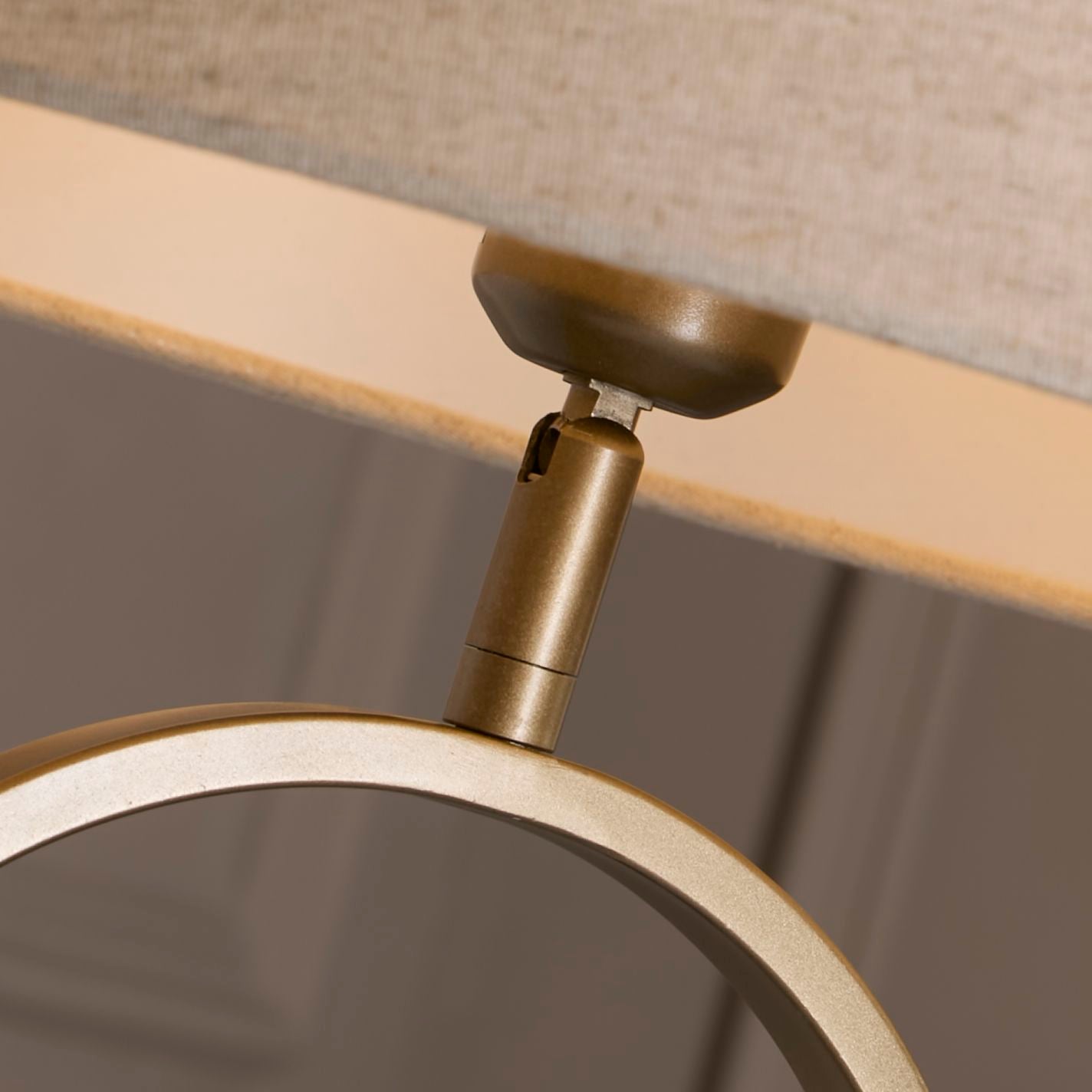 Close up of the bronze table lamp's swivel neck joint, showing where the oval ring base meets the natural linen shade