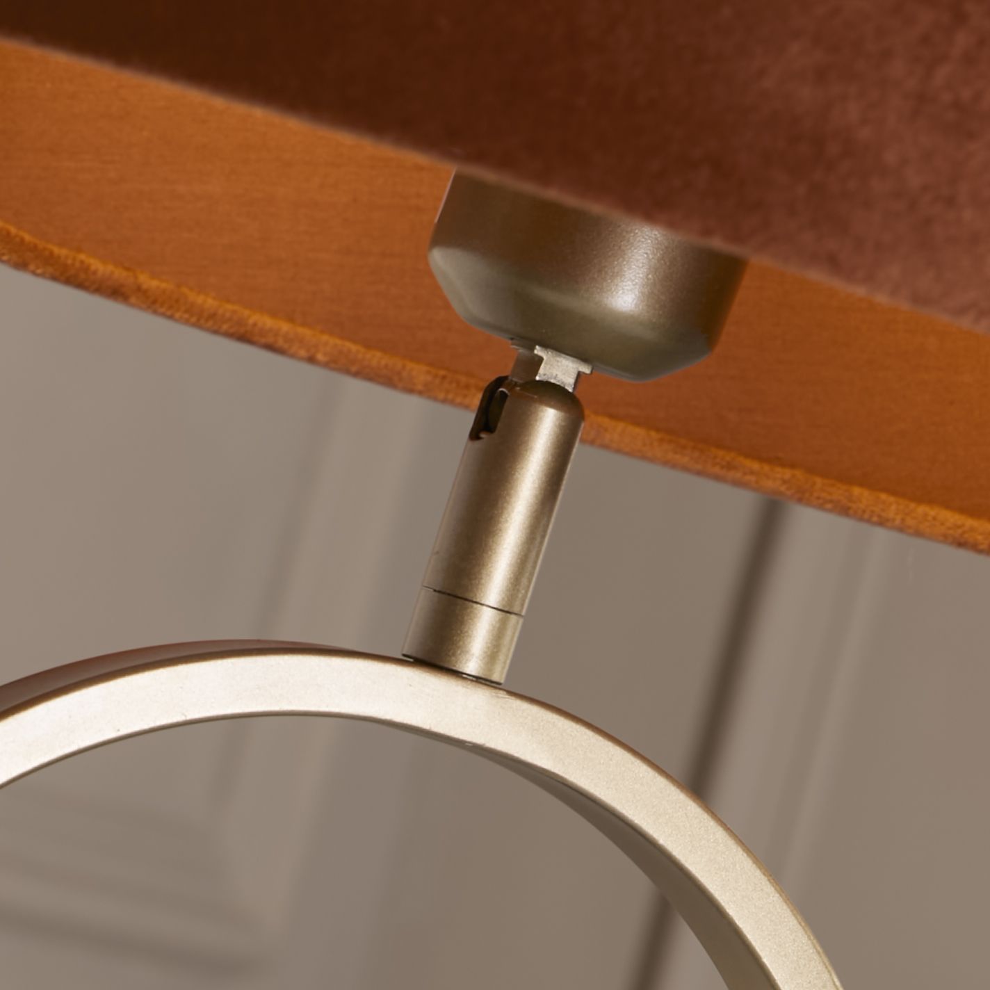 Close up of the bronze table lamp's swivel neck joint, showing where the oval ring base meets the burnt orange velvet shade