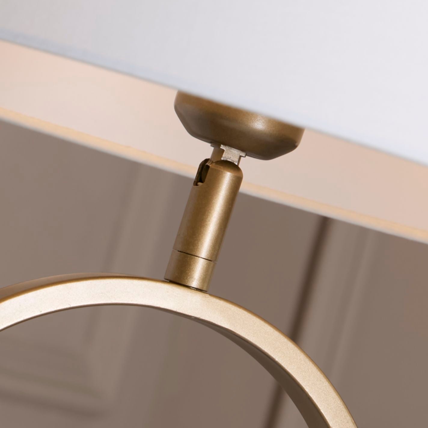 Close up of the bronze table lamp's swivel neck joint, showing where the oval ring base meets the white cotton shade