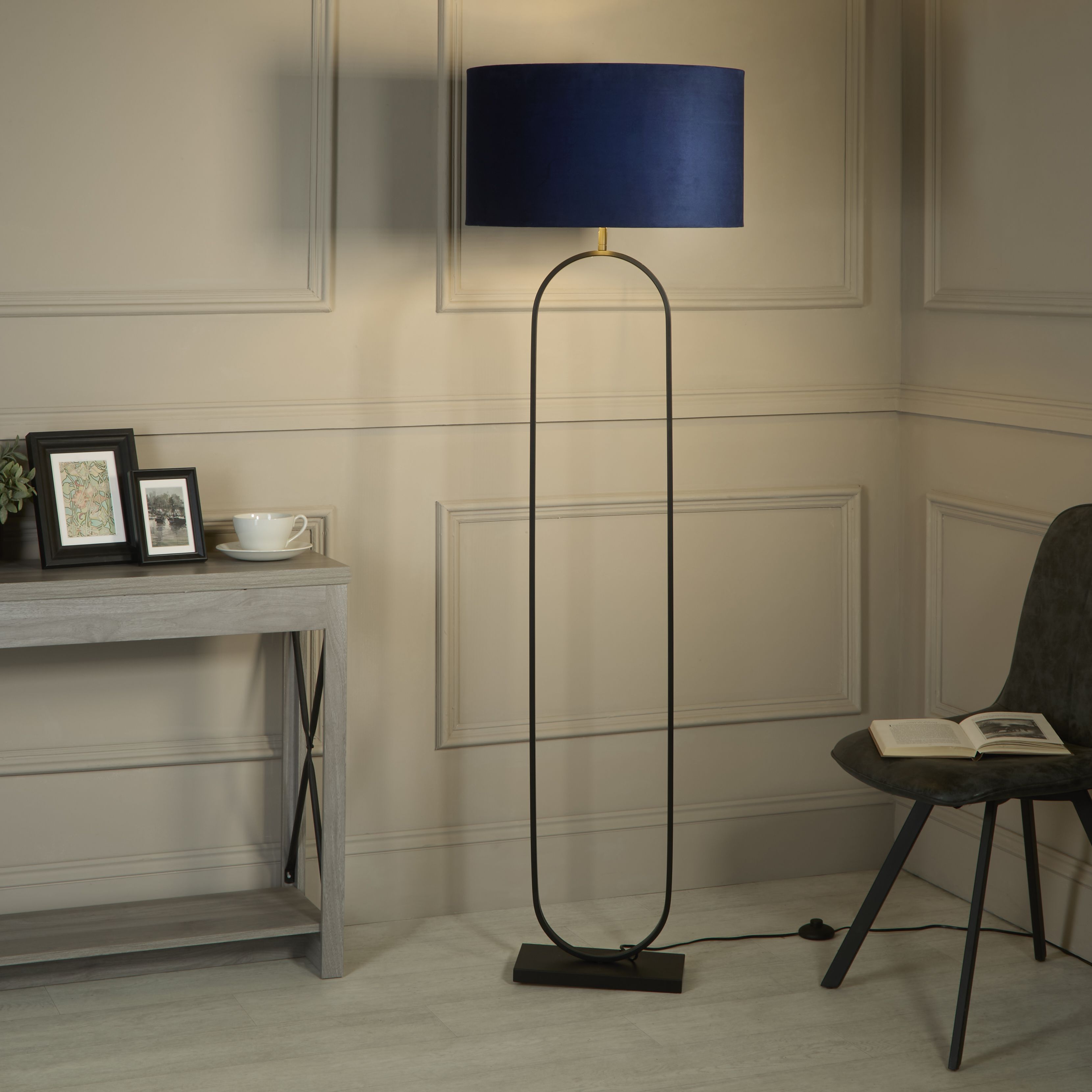 Modish floor lamp with navy velvet shade styled in a panelled living room beside a console table and a black armchair
