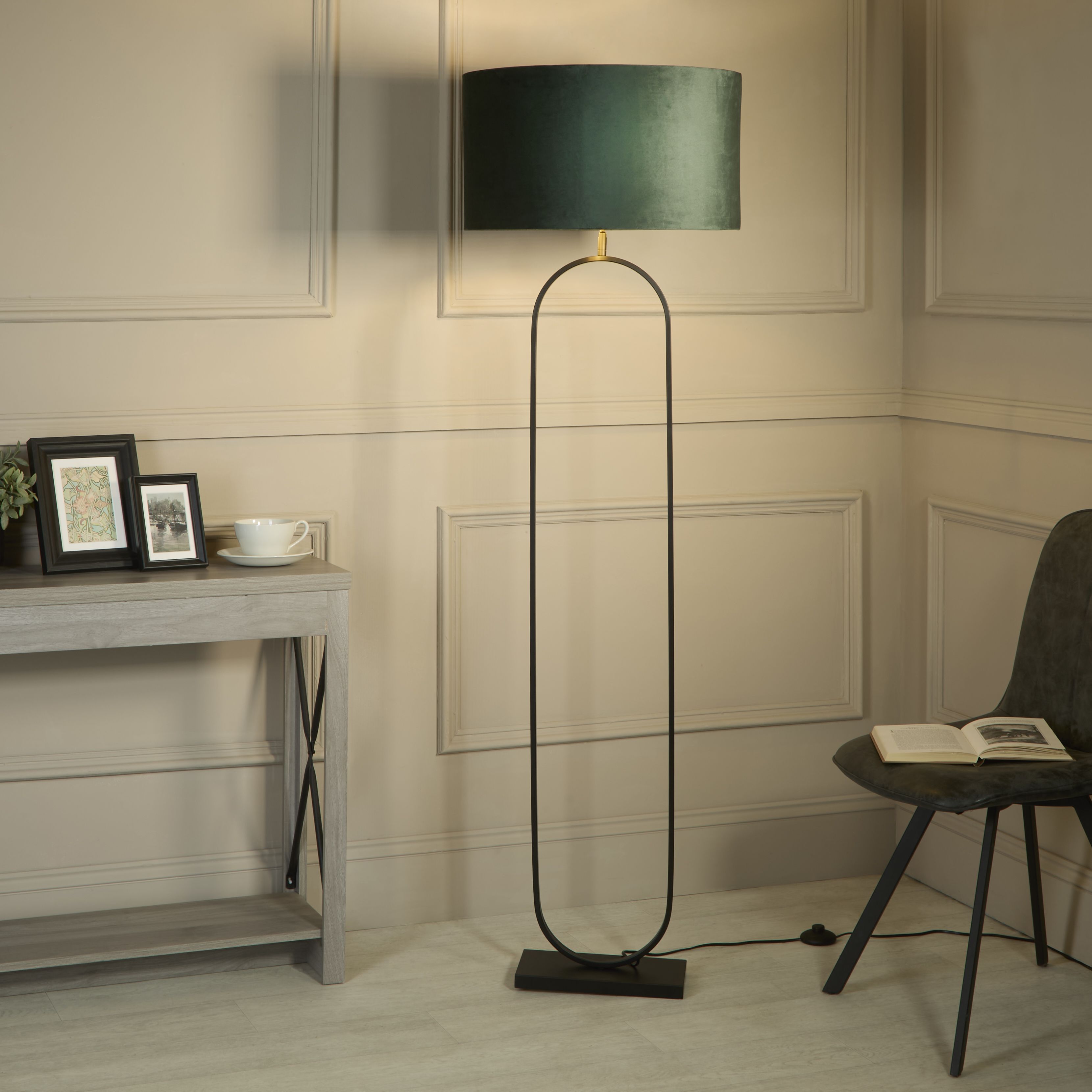 Modish floor lamp with green velvet shade styled in a living room corner beside a console table and a black chair with an open book