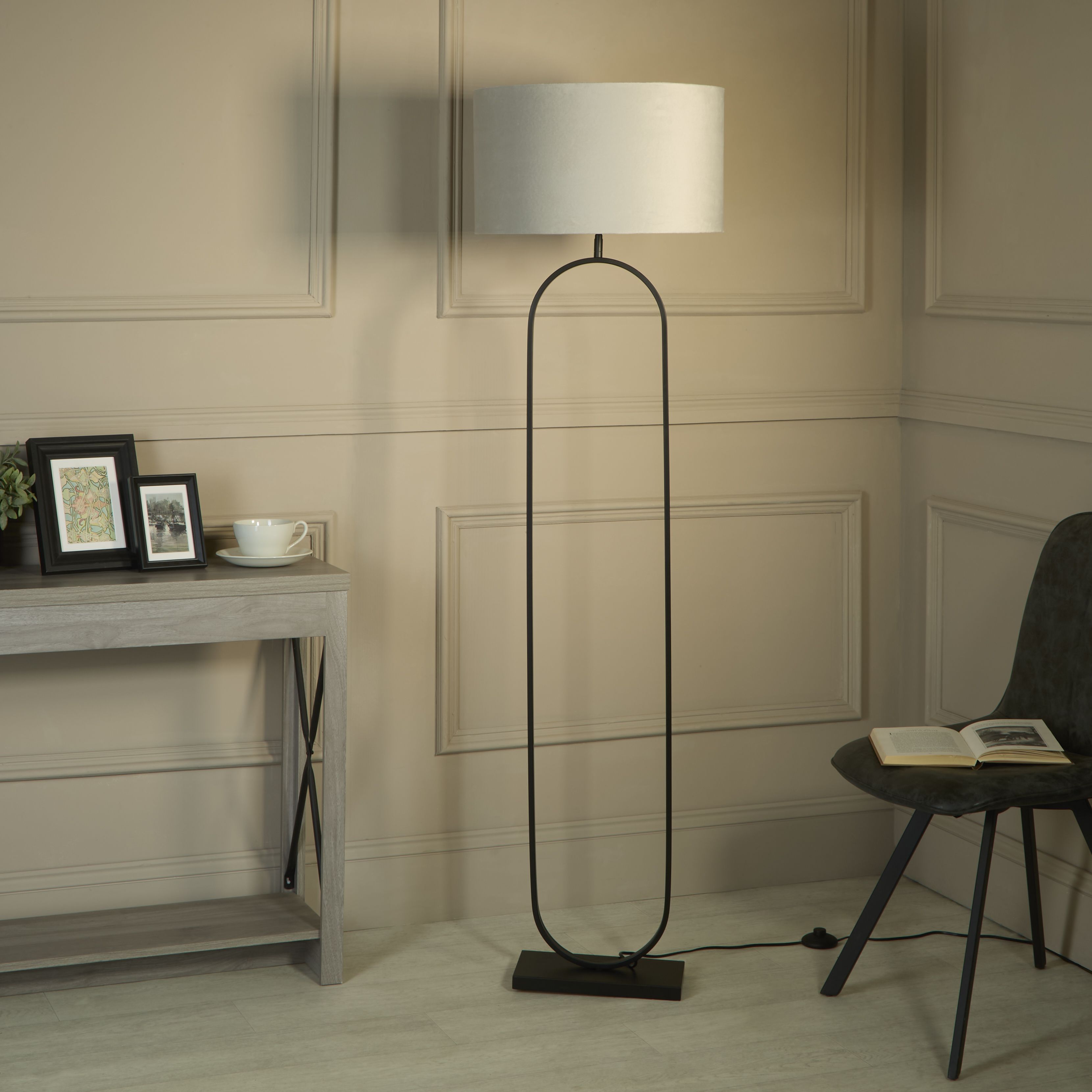 Modish floor lamp with light grey velvet shade styled in a living room corner beside a console table and a black chair with an open book
