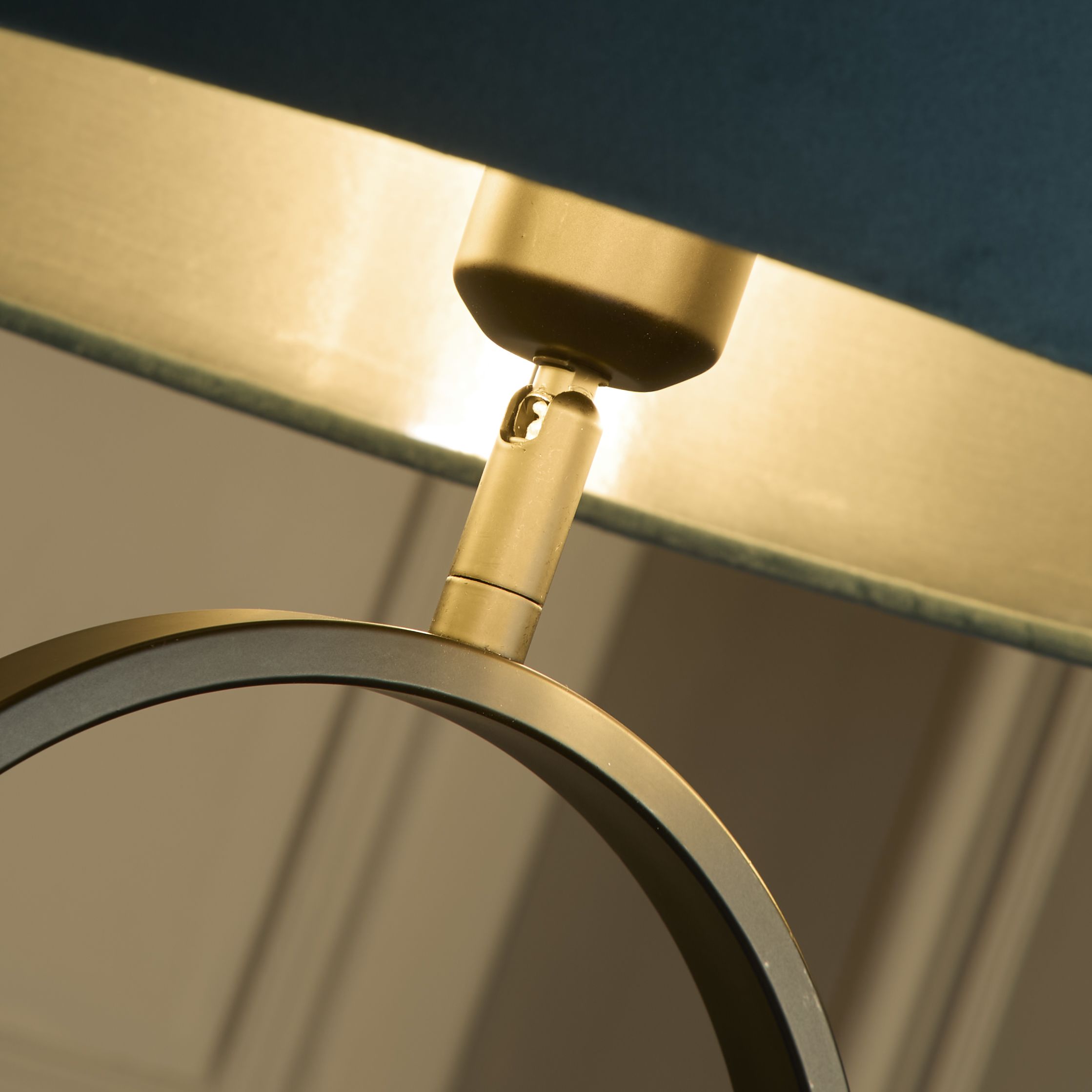 Close up of the brass adjustable joint connecting the teal velvet shade to the black oval ring base