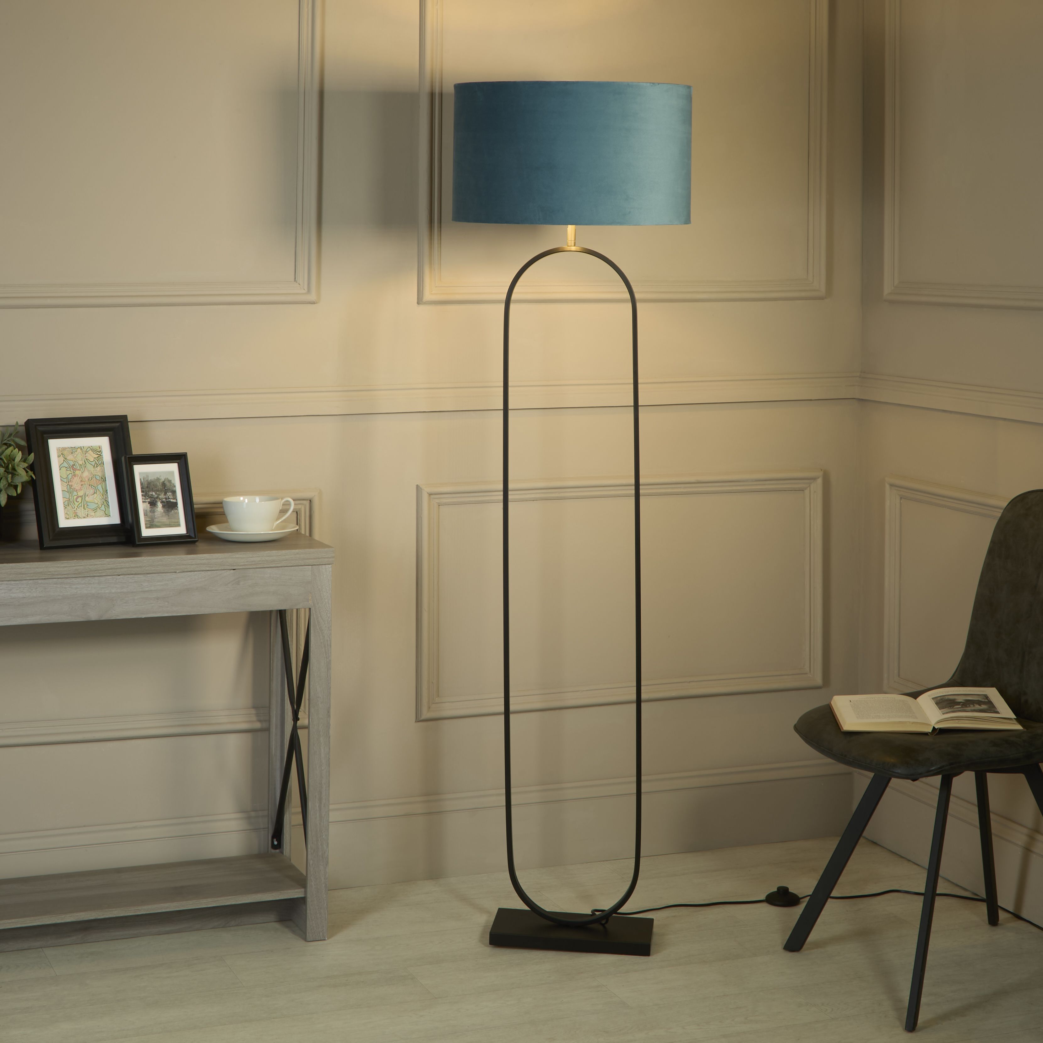 Modish floor lamp with teal velvet shade styled in a living room corner beside a console table and a black chair with an open book