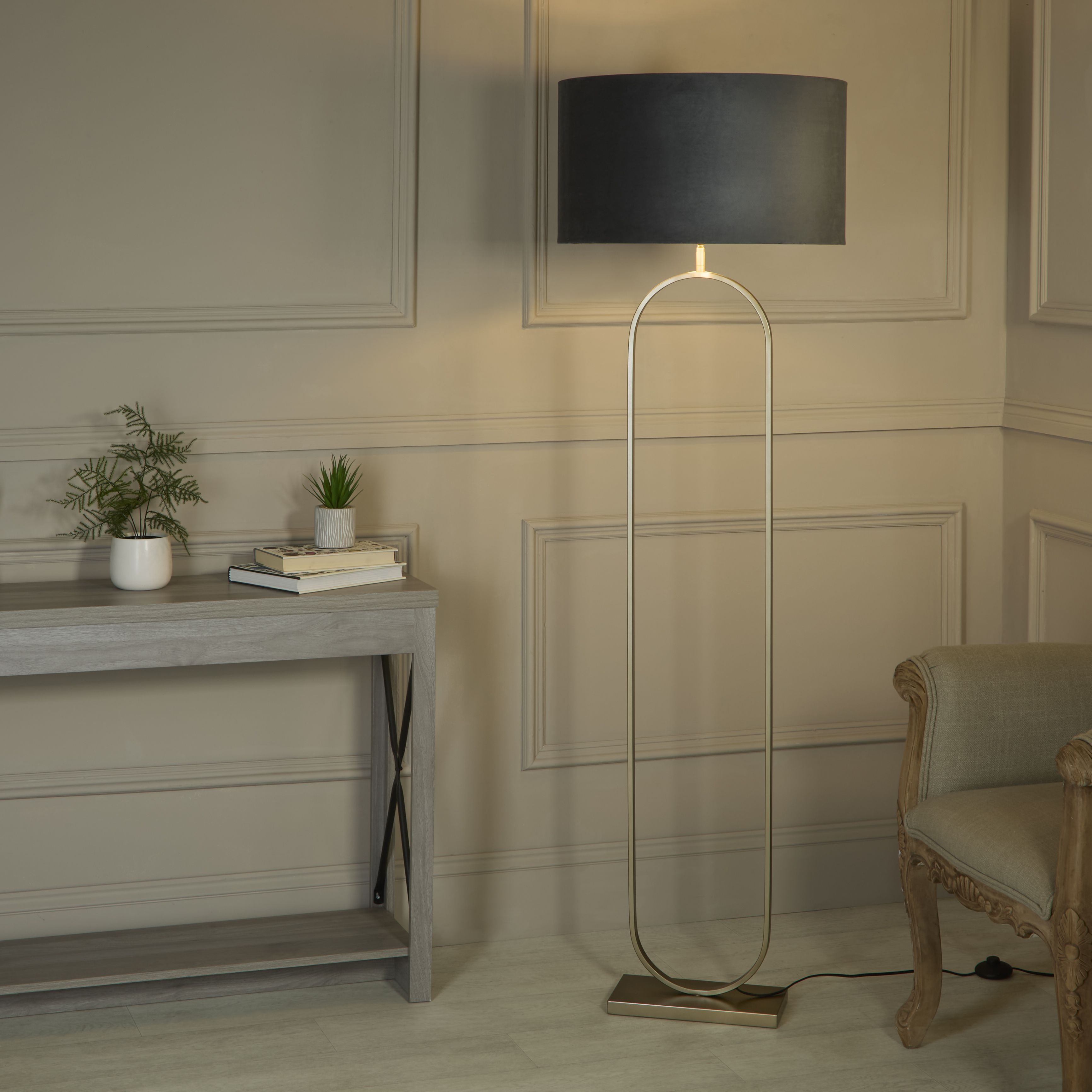 Searchlight Modish floor lamp with dark charcoal grey velvet shade switched on beside a console table and armchair in a panelled hallway
