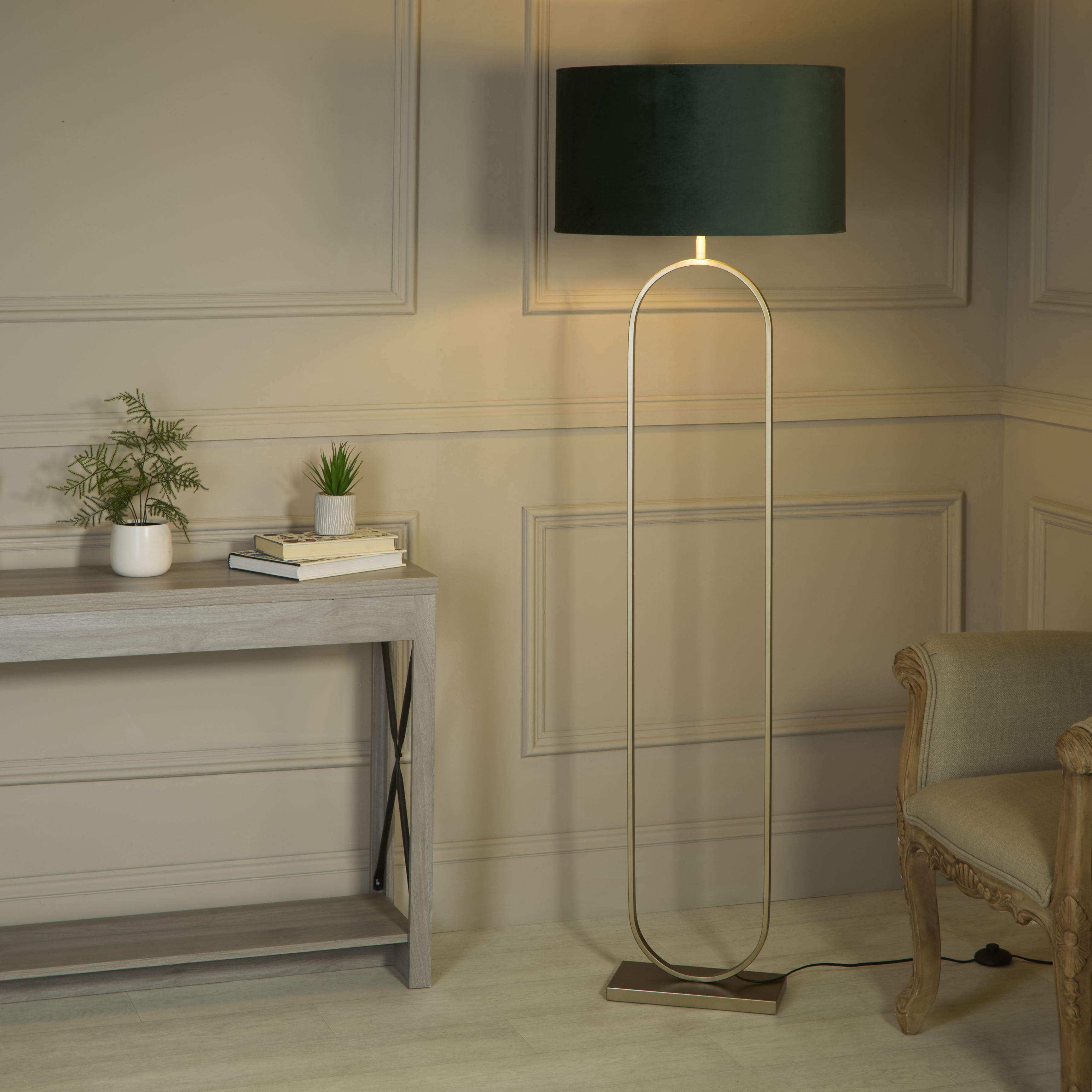 Searchlight Modish floor lamp with forest green velvet shade switched on beside a console table and armchair in a panelled hallway