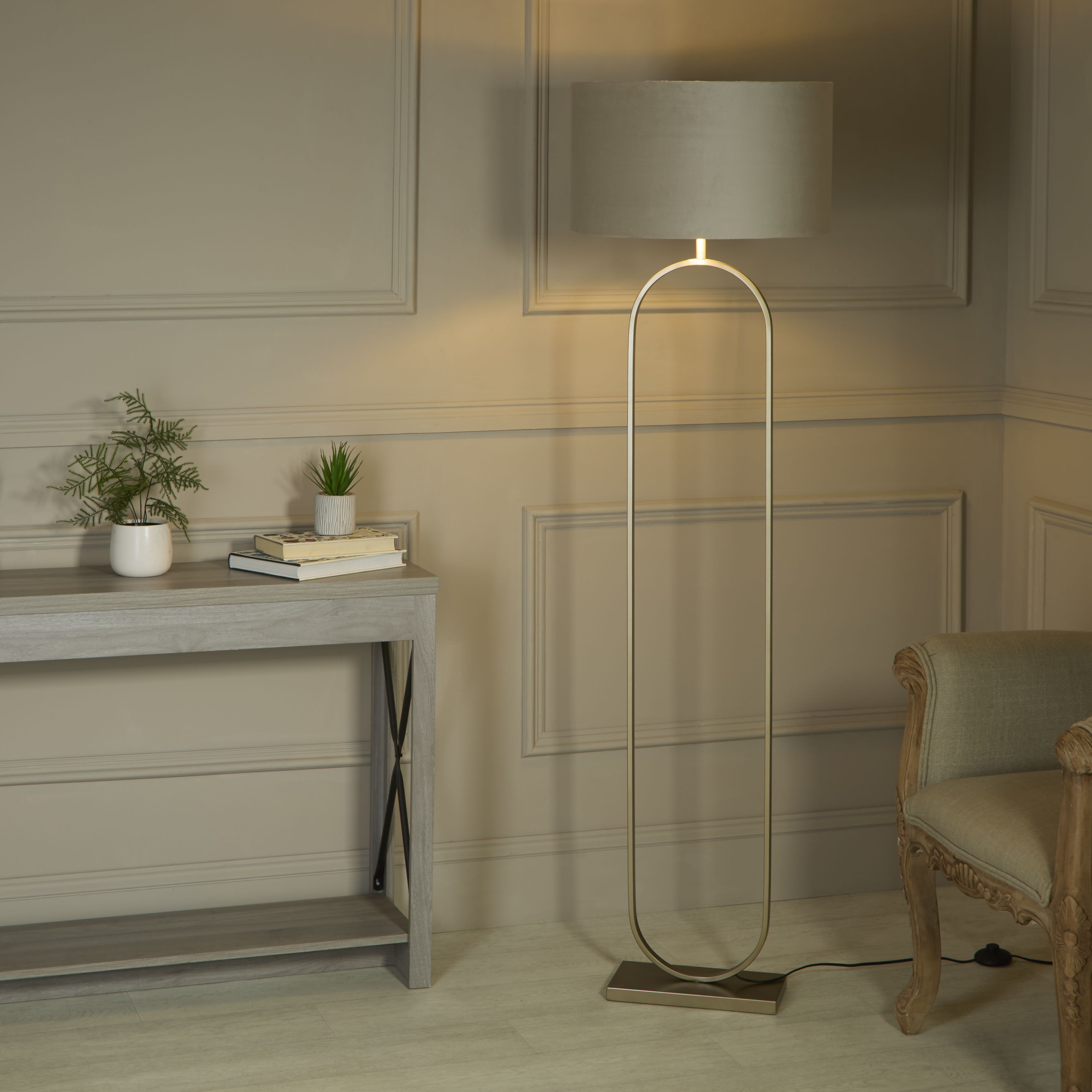 Modish floor lamp with taupe velvet shade styled beside a console table with plants and books in a panelled living room