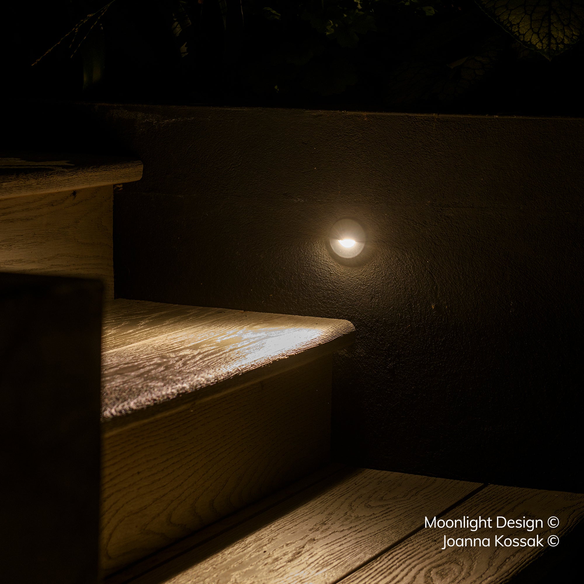 A Hunza Euro eyelid light recessed into a rendered wall base beside garden steps, lighting the step and grass at night. A Moonlight Design installation, not stock imagery.