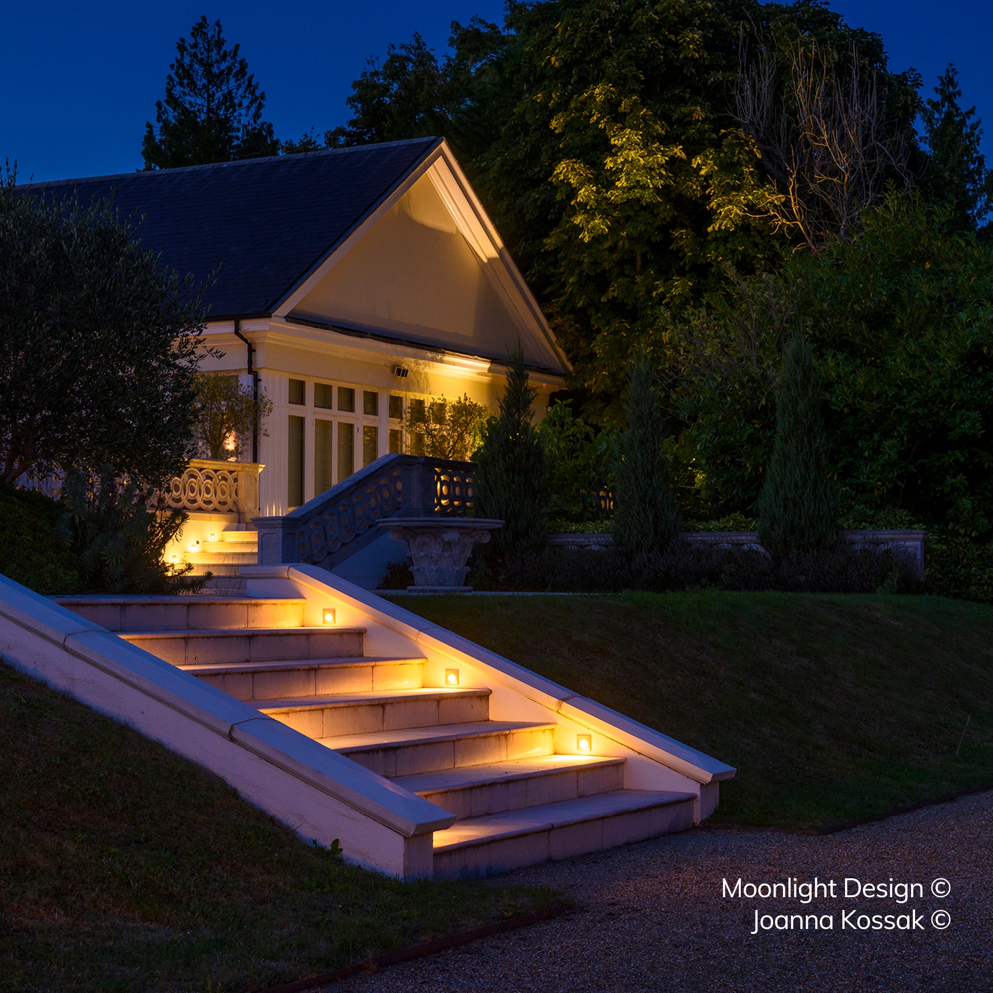 Louvred step lights recessed into a run of stone steps outside a garden pavilion, casting a wide horizontal wash of light across each tread at dusk. A Moonlight Design installation, not stock imagery.