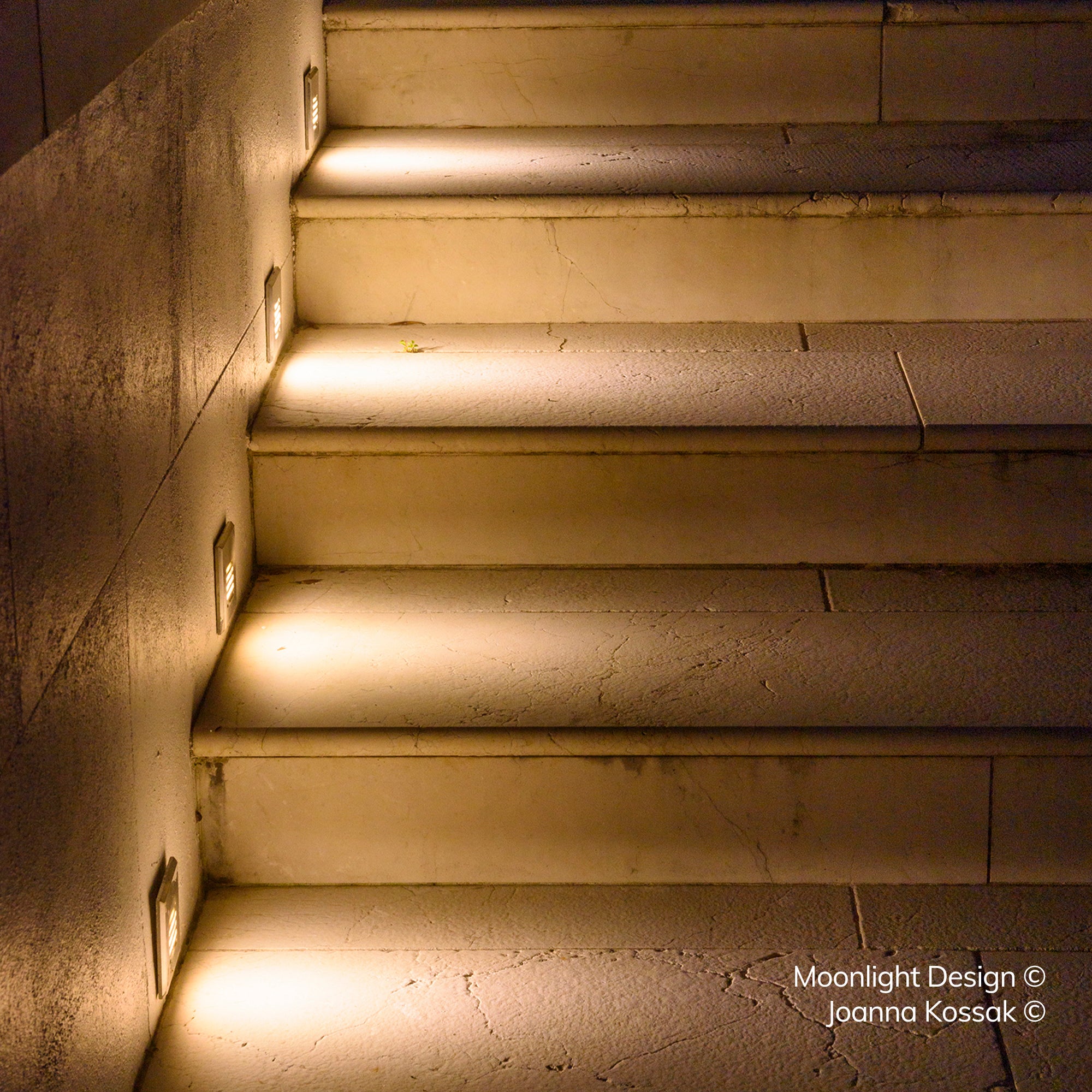 Close up looking down a run of stone steps lit by recessed louvred step lights, each throwing an even band of light across the tread and riser above. A Moonlight Design installation, not stock imagery.