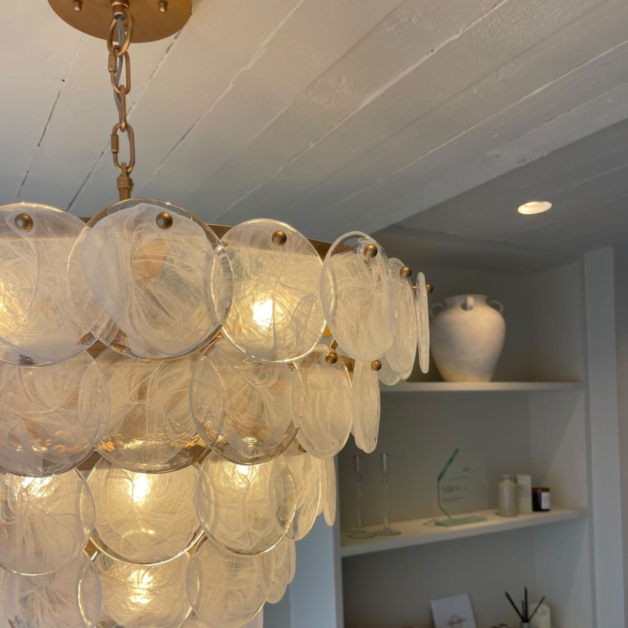 Utopia Scale 9 Light Pendant Chandelier lit in a styled room, close view of the tiered glass discs beside a vase and open shelving