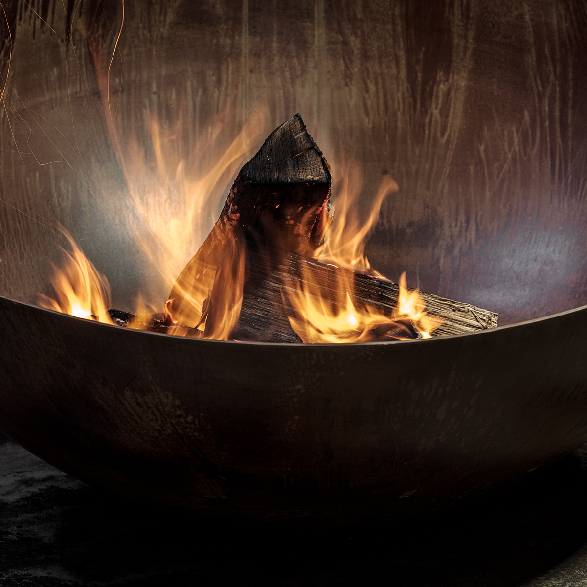 Close-up of burning firewood and orange flames inside the GlammFire Solace Corten steel outdoor fire pit