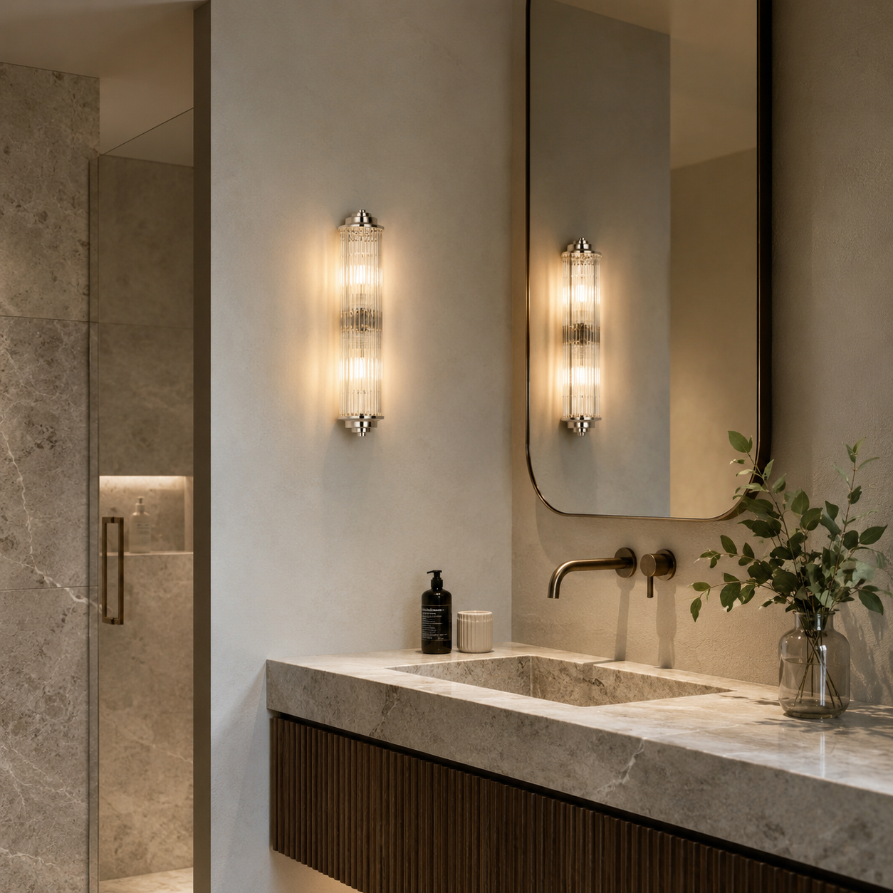 Polished nickel ribbed glass wall light installed beside a bathroom mirror in a luxury contemporary bathroom.
